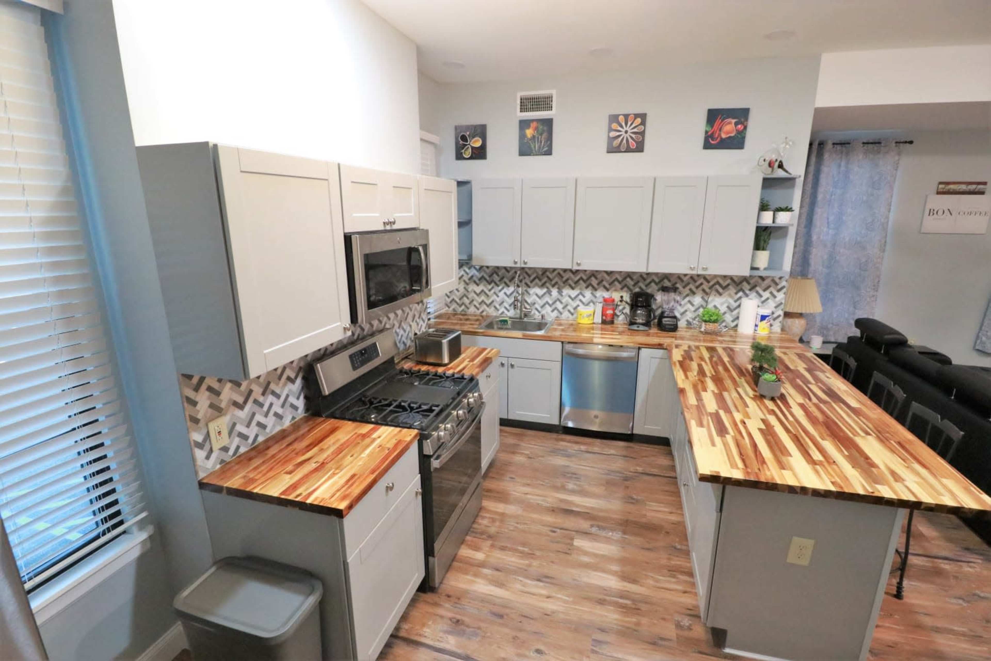 A modern kitchen features light gray cabinets, stainless steel appliances, and a wooden countertop with a chevron-patterned backsplash.