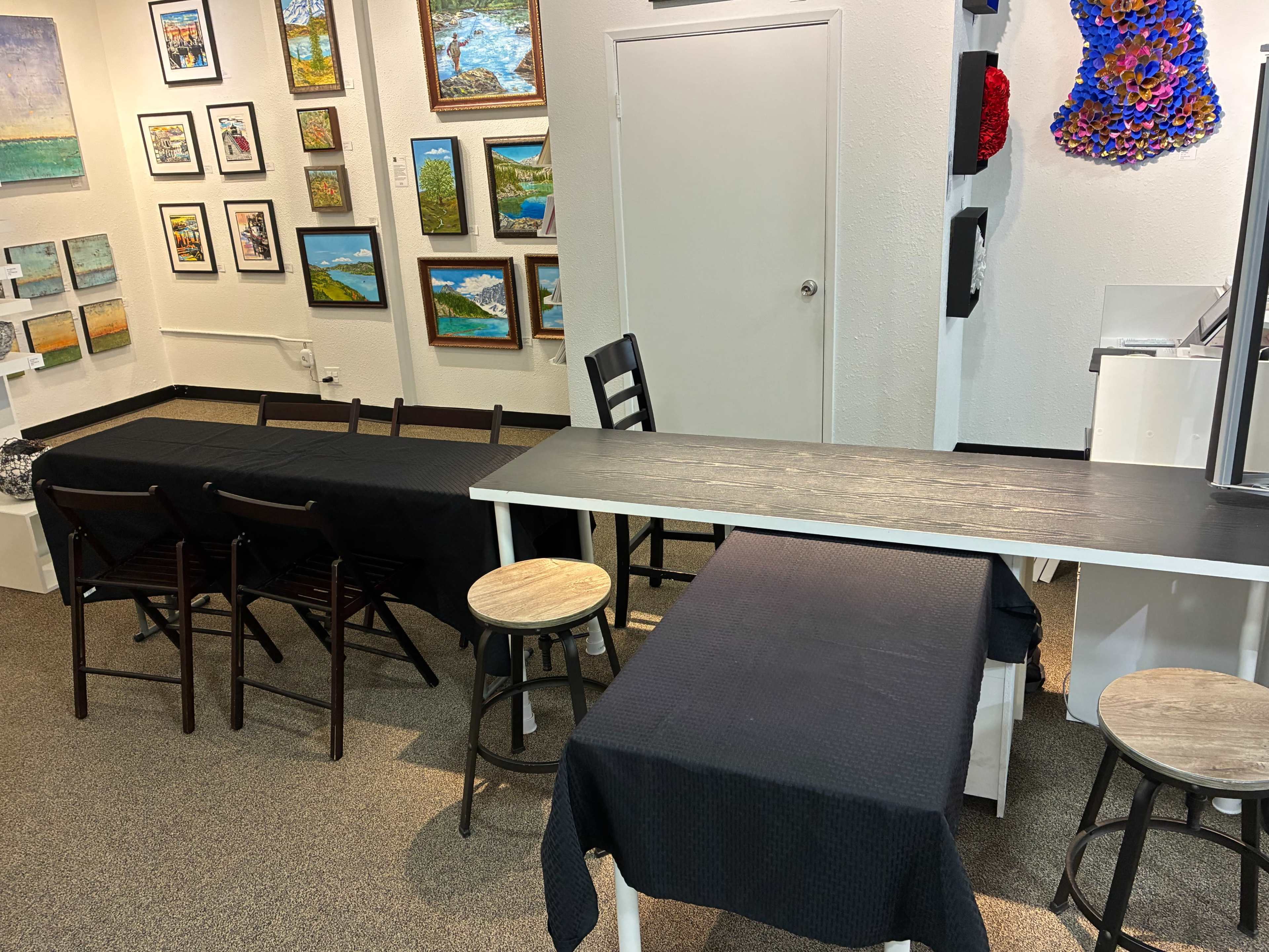 The image shows a room with multiple tables covered in black cloth, surrounded by chairs and framed artwork on the walls.