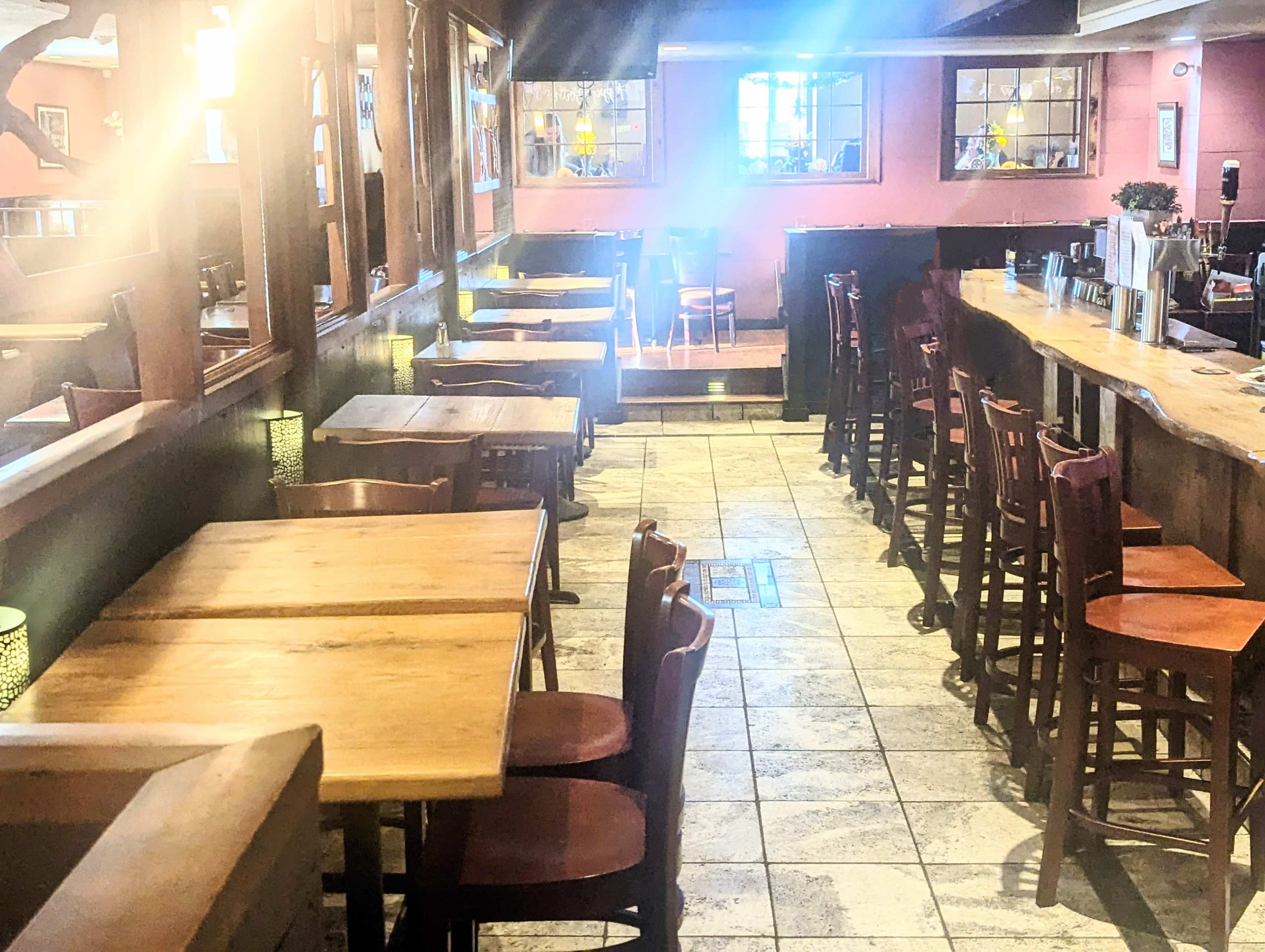 An interior view of a restaurant featuring rows of wooden tables and chairs, with a bar area in the background.