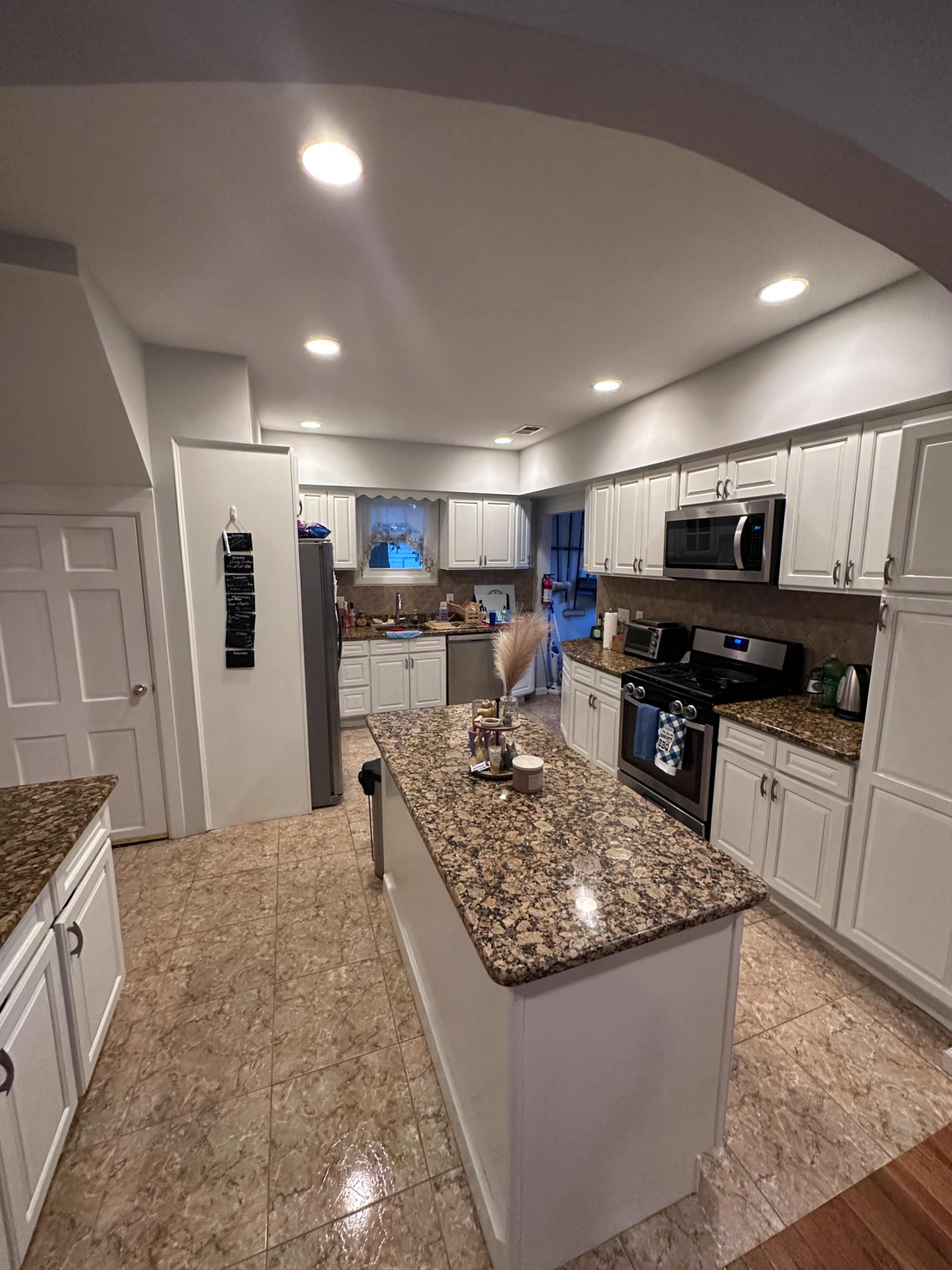 The image shows a modern kitchen with granite countertops, white cabinets, and stainless steel appliances, featuring an island in the center.