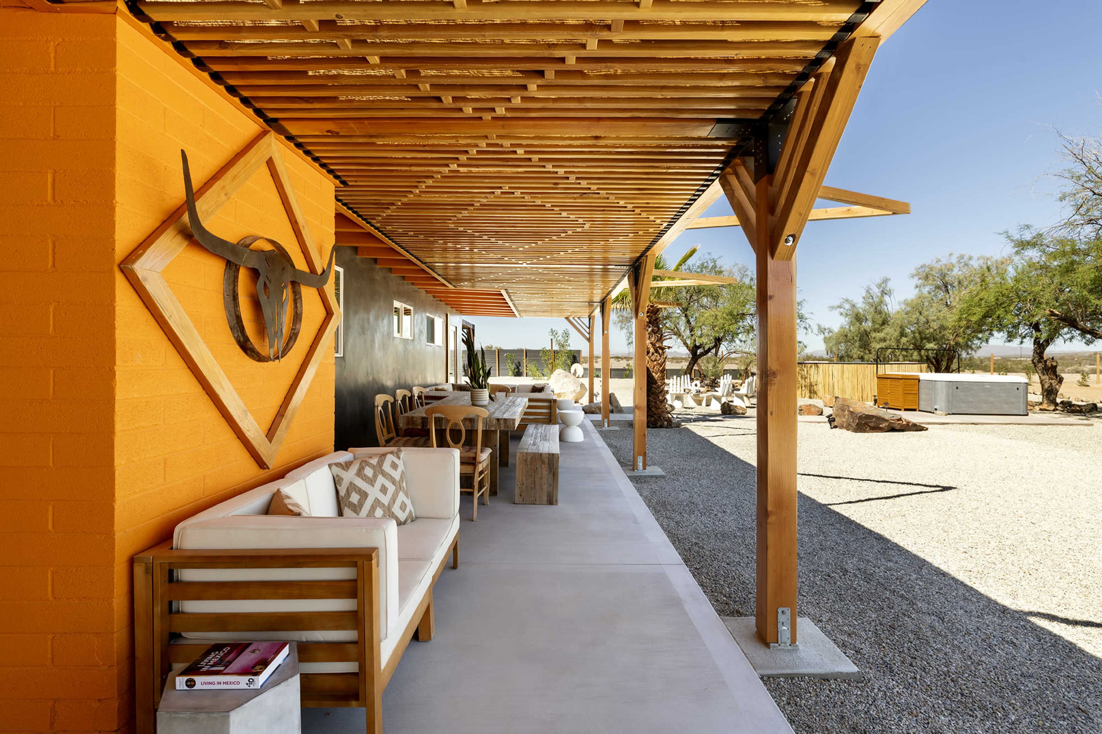 A modern outdoor seating area with wooden furniture, a textured wall with a geometric design, and a gravel pathway leading to a spacious outdoor space.