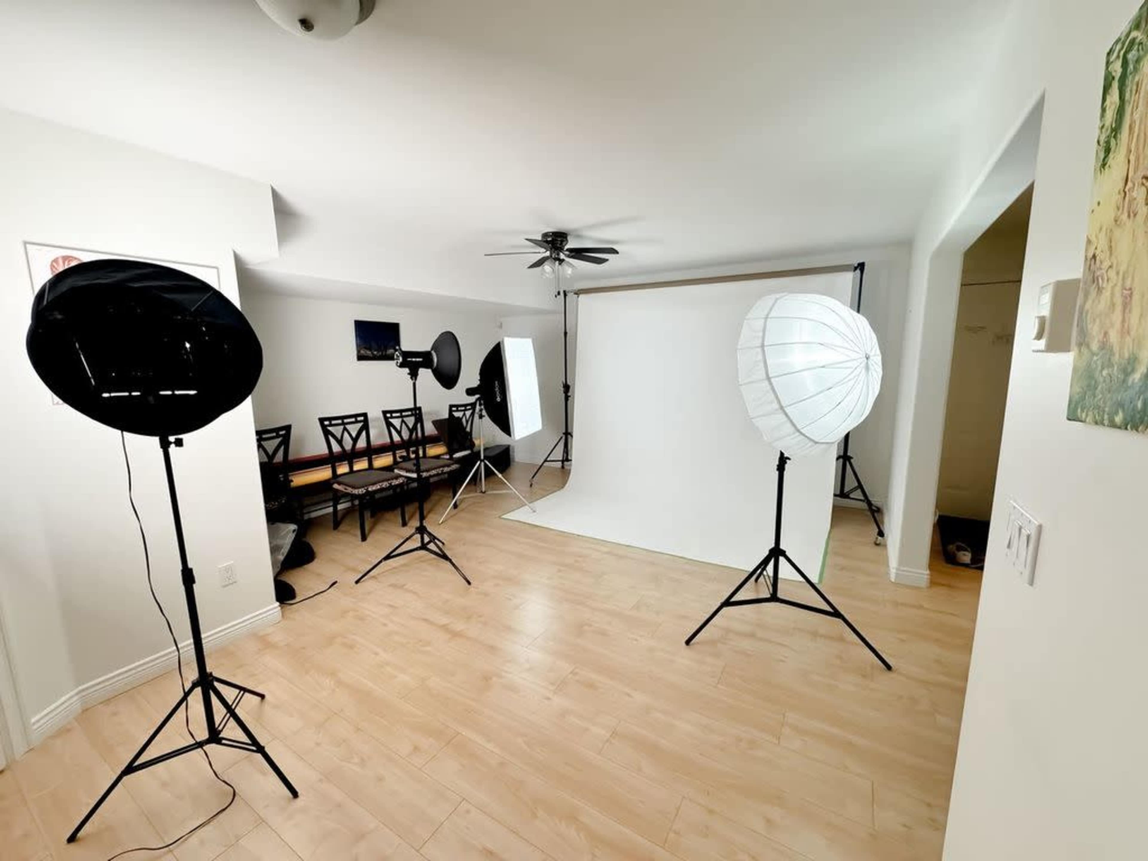 The image shows a well-lit studio setup with two softbox lights, a backdrop, and a dining table with chairs in a spacious room.