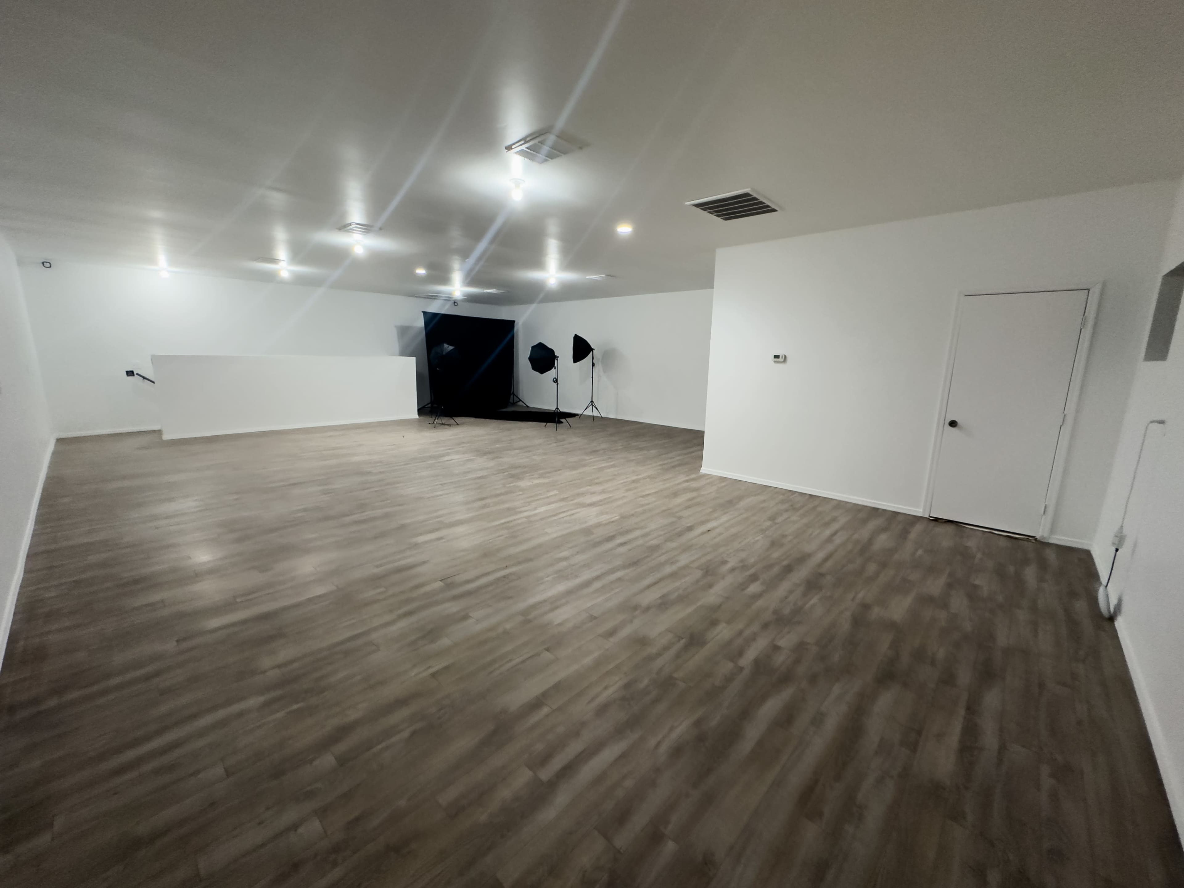 A spacious, empty room with polished wooden flooring, dimmed lighting, and a backdrop set up for photography.