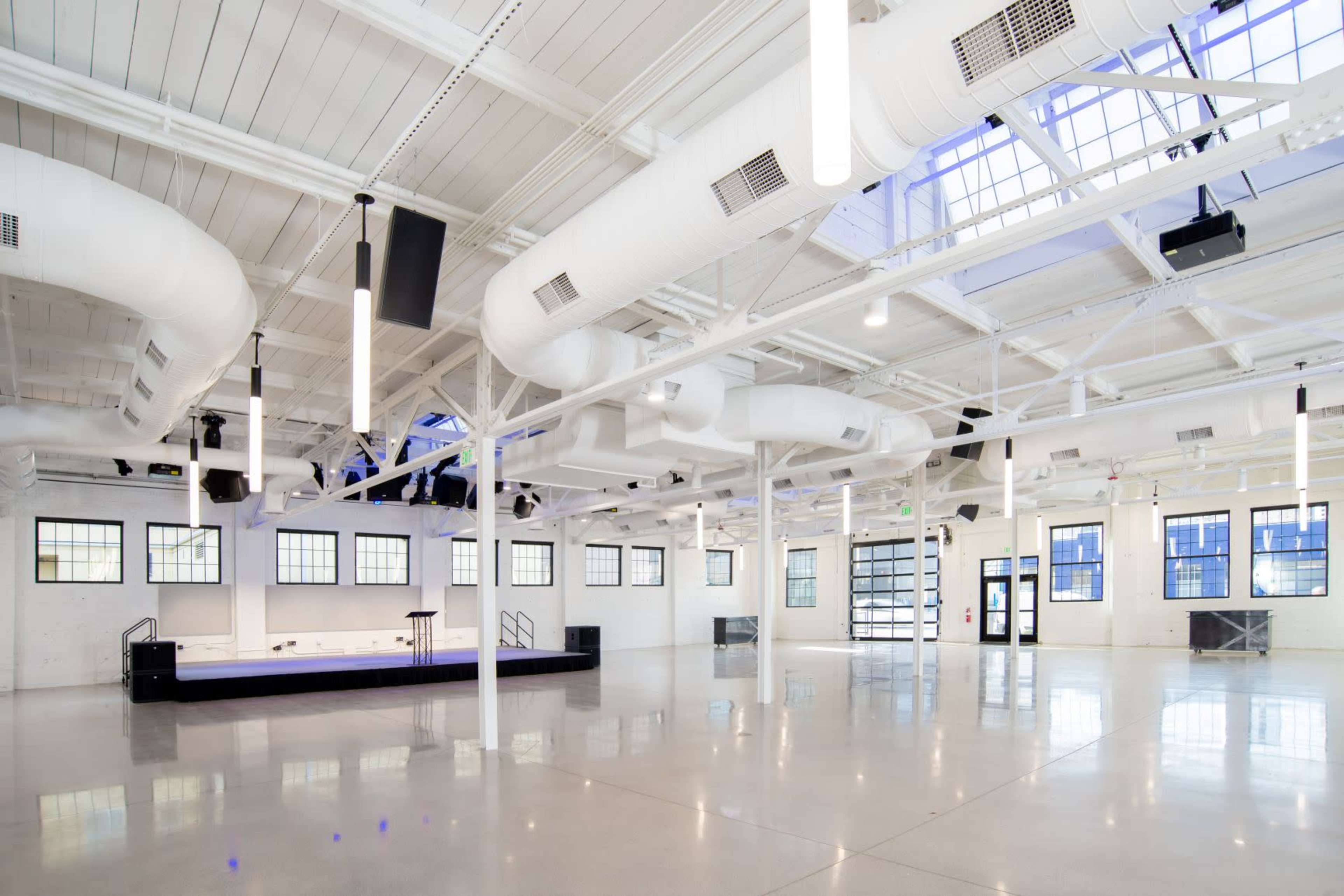 A spacious, modern event venue with high ceilings, large windows, and exposed ductwork.