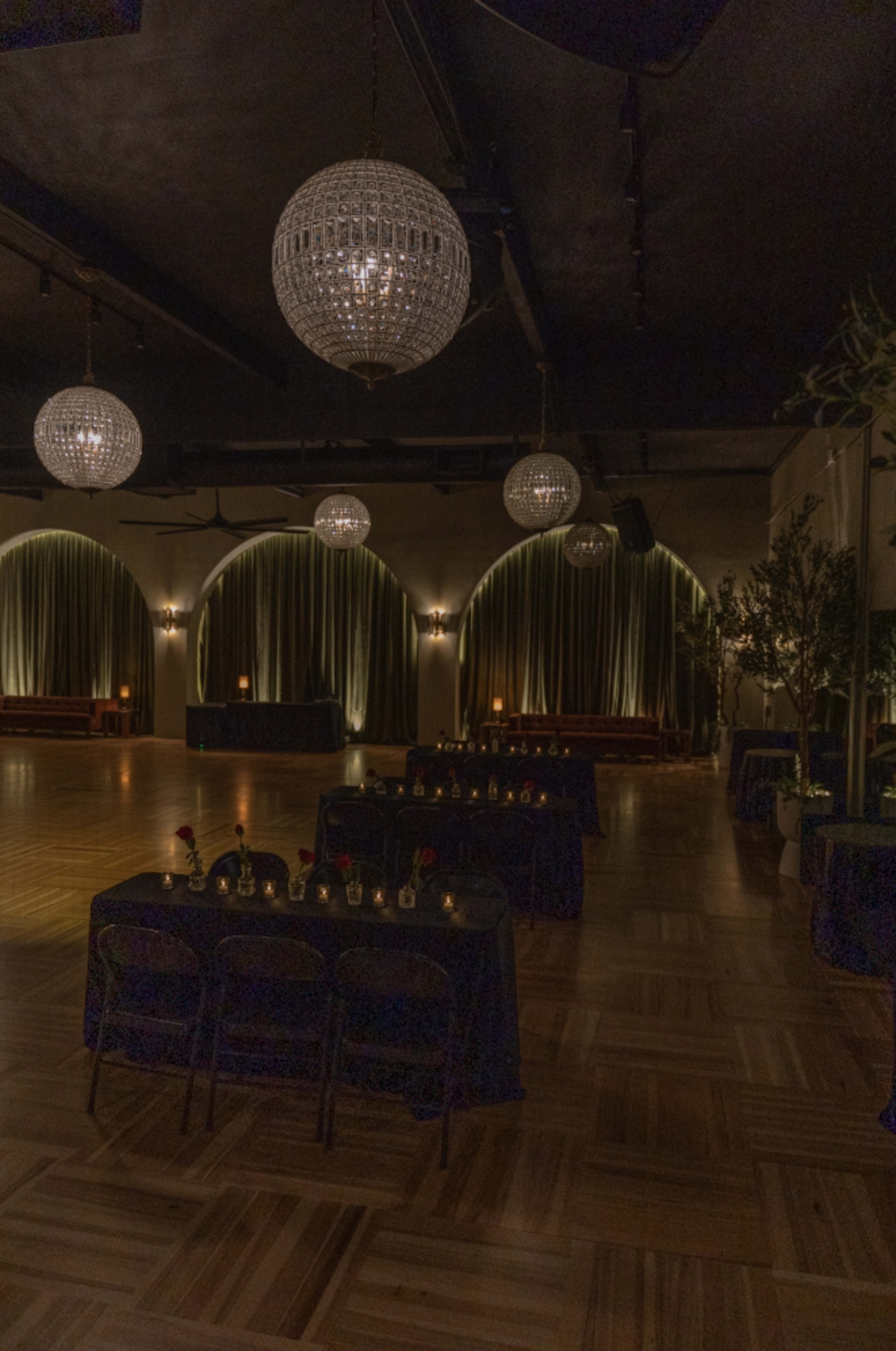 An elegantly arranged event space with multiple tables set up, sparkling chandeliers hanging from the ceiling, and soft lighting illuminating the room.