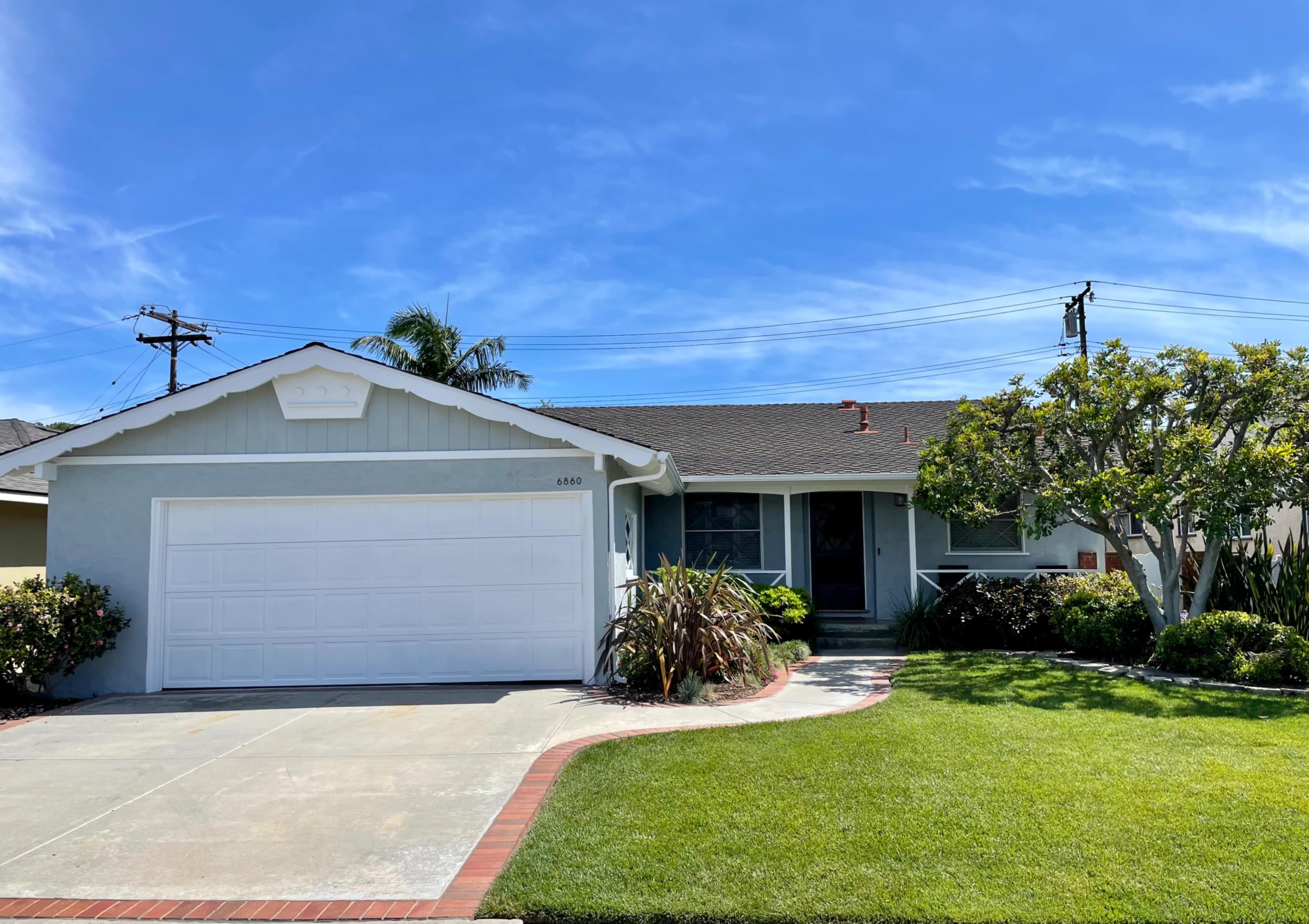 A single-story house with a white garage door, surrounded by neatly trimmed grass and shrubs, under a clear blue sky.