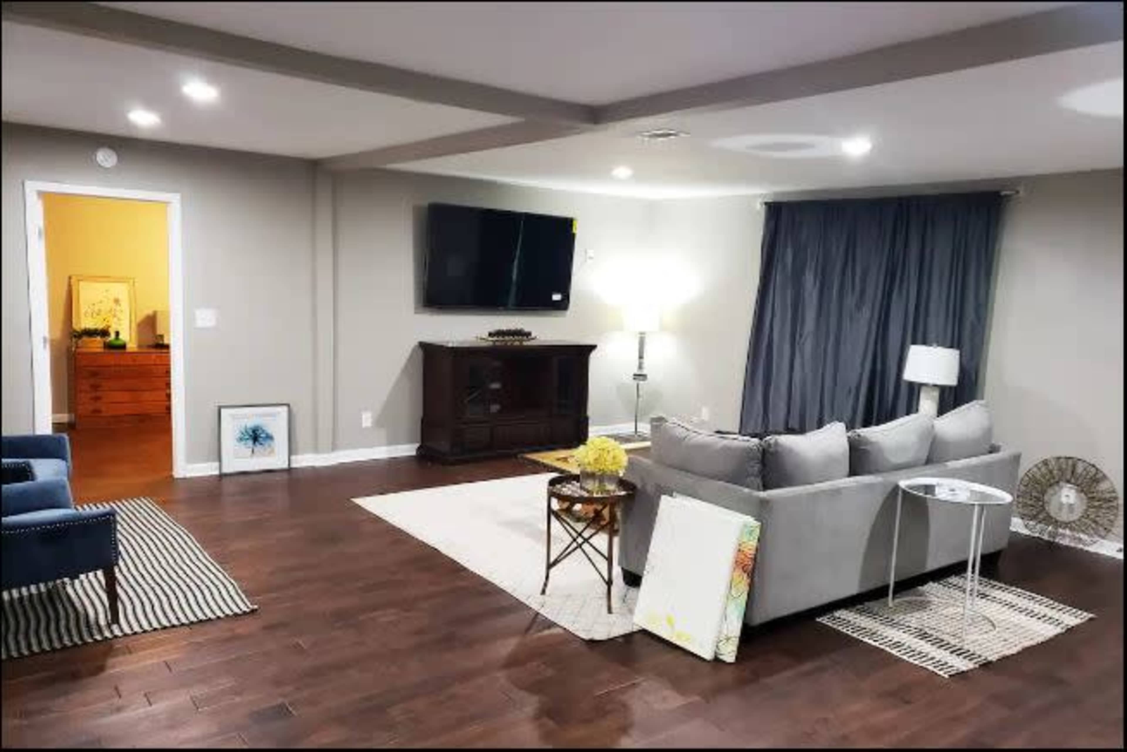 A modern living room with a gray couch, a TV mounted on the wall, a floor lamp, and a side table beside a decorative rug.