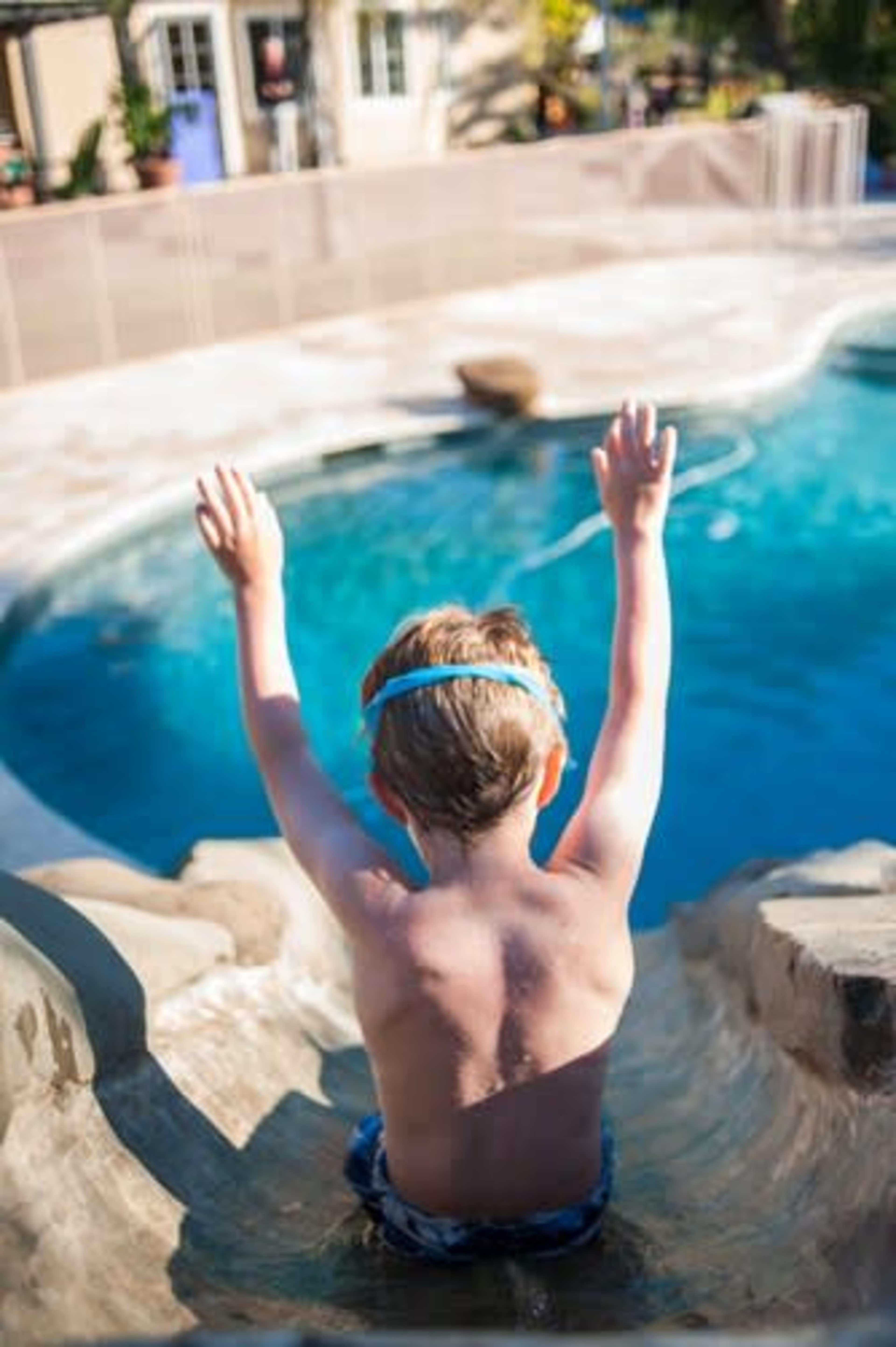 A young boy sits on a water slide, poised to enter a swimming pool.