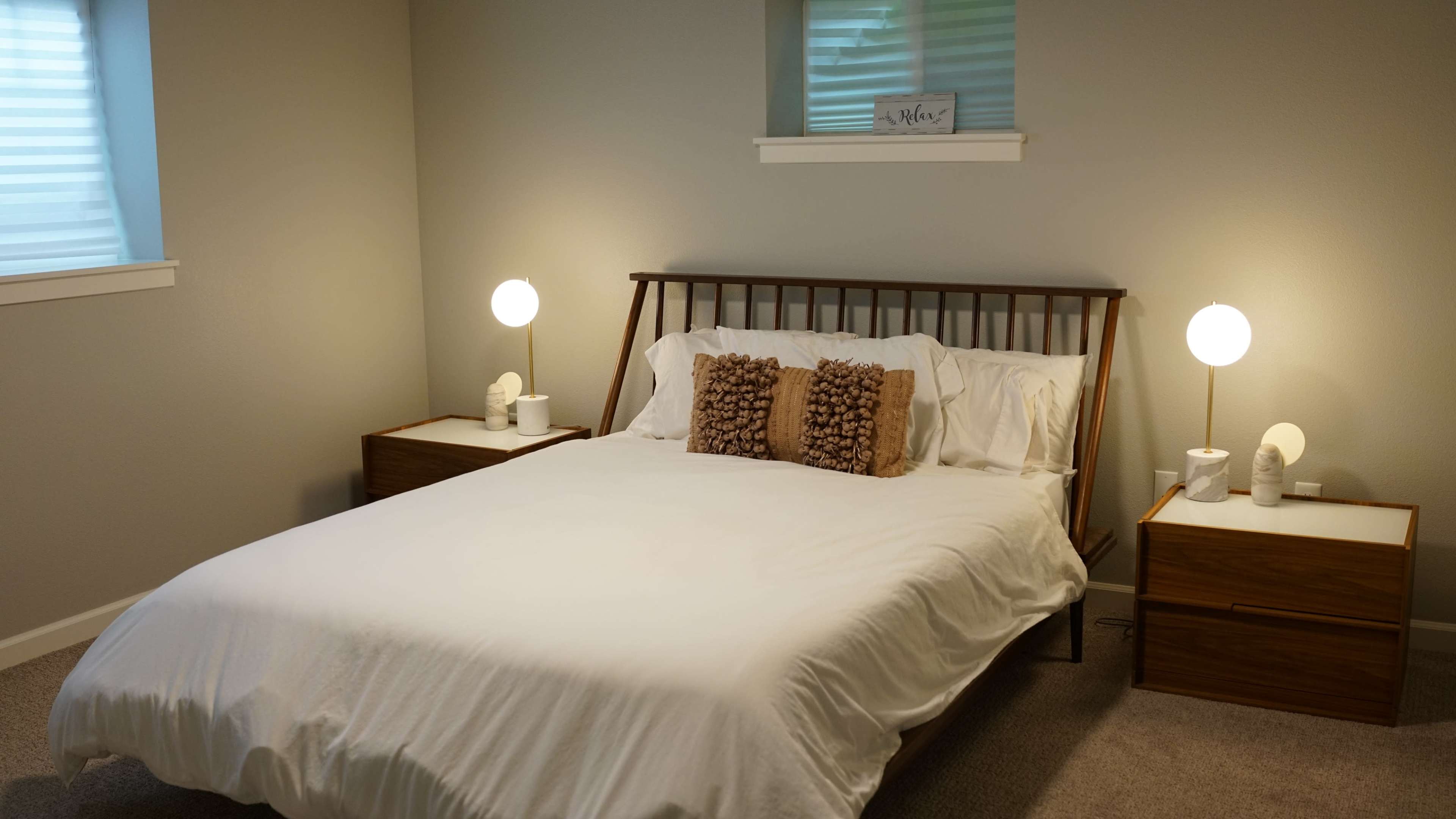 A minimalist bedroom features a bed with white bedding, flanked by two wooden nightstands with lamps.