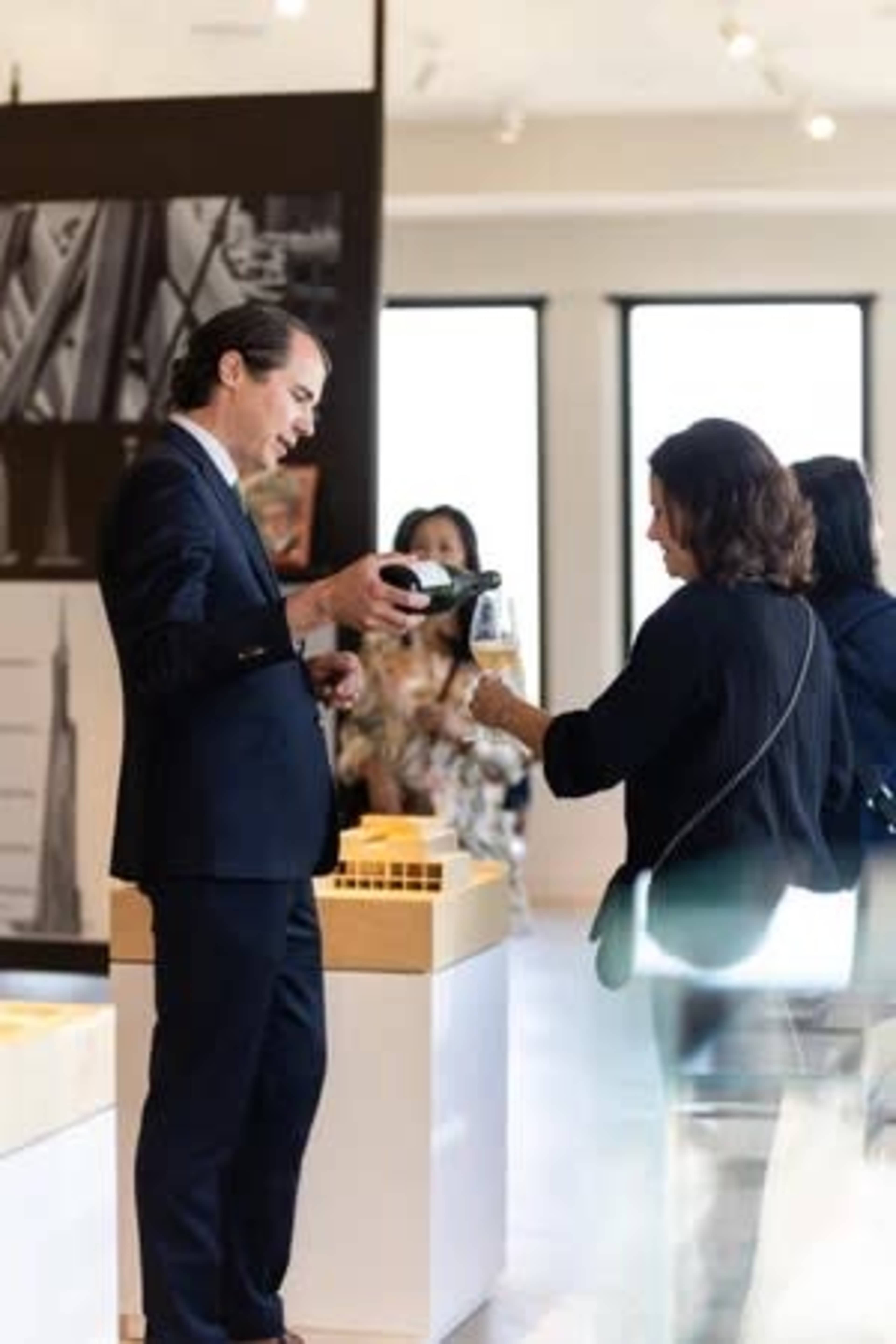 A man in a suit hands a drink to a woman in a black top at an art exhibit.