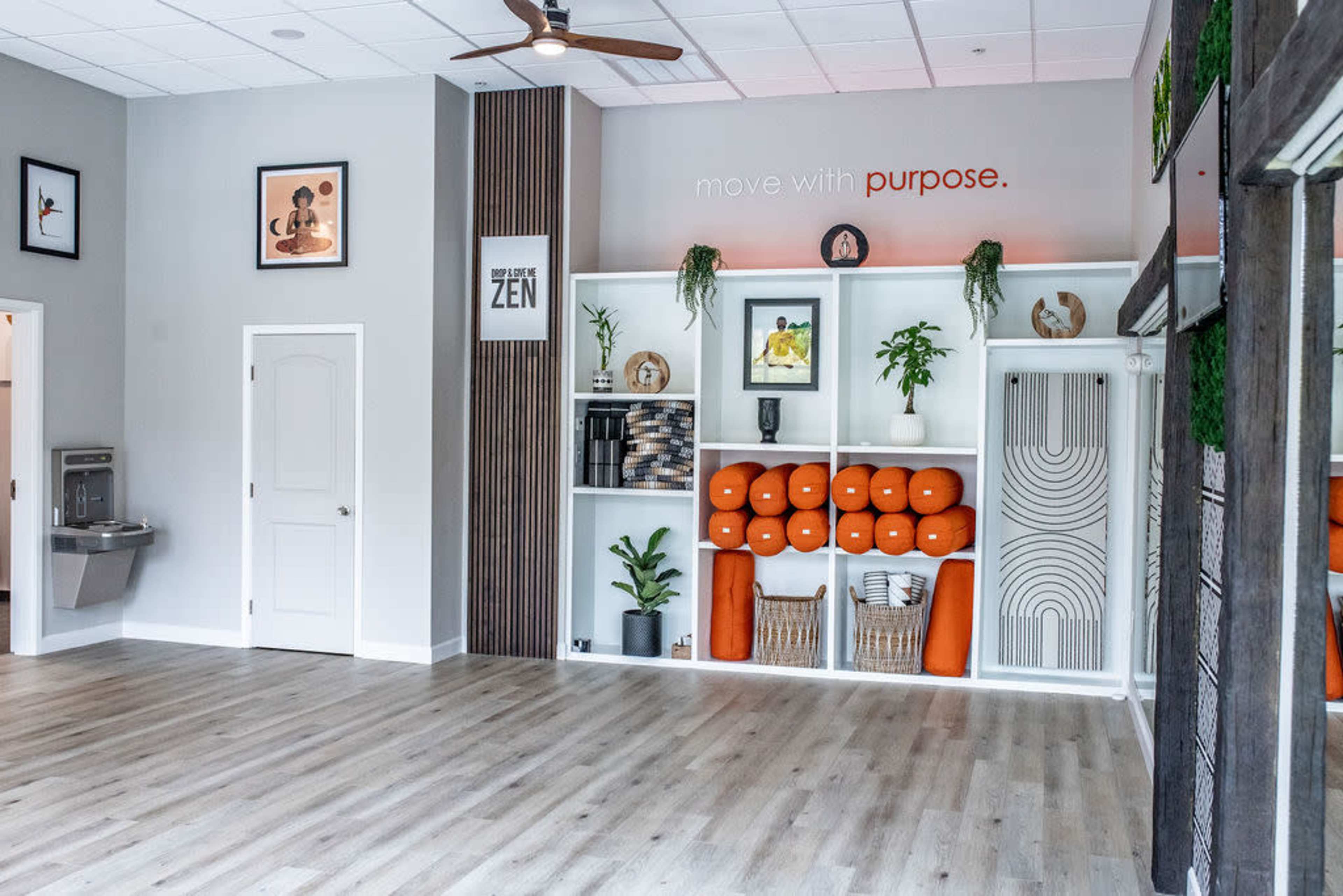 A bright, minimalist studio space with shelves containing plants and fitness equipment, complemented by a large, open floor area.