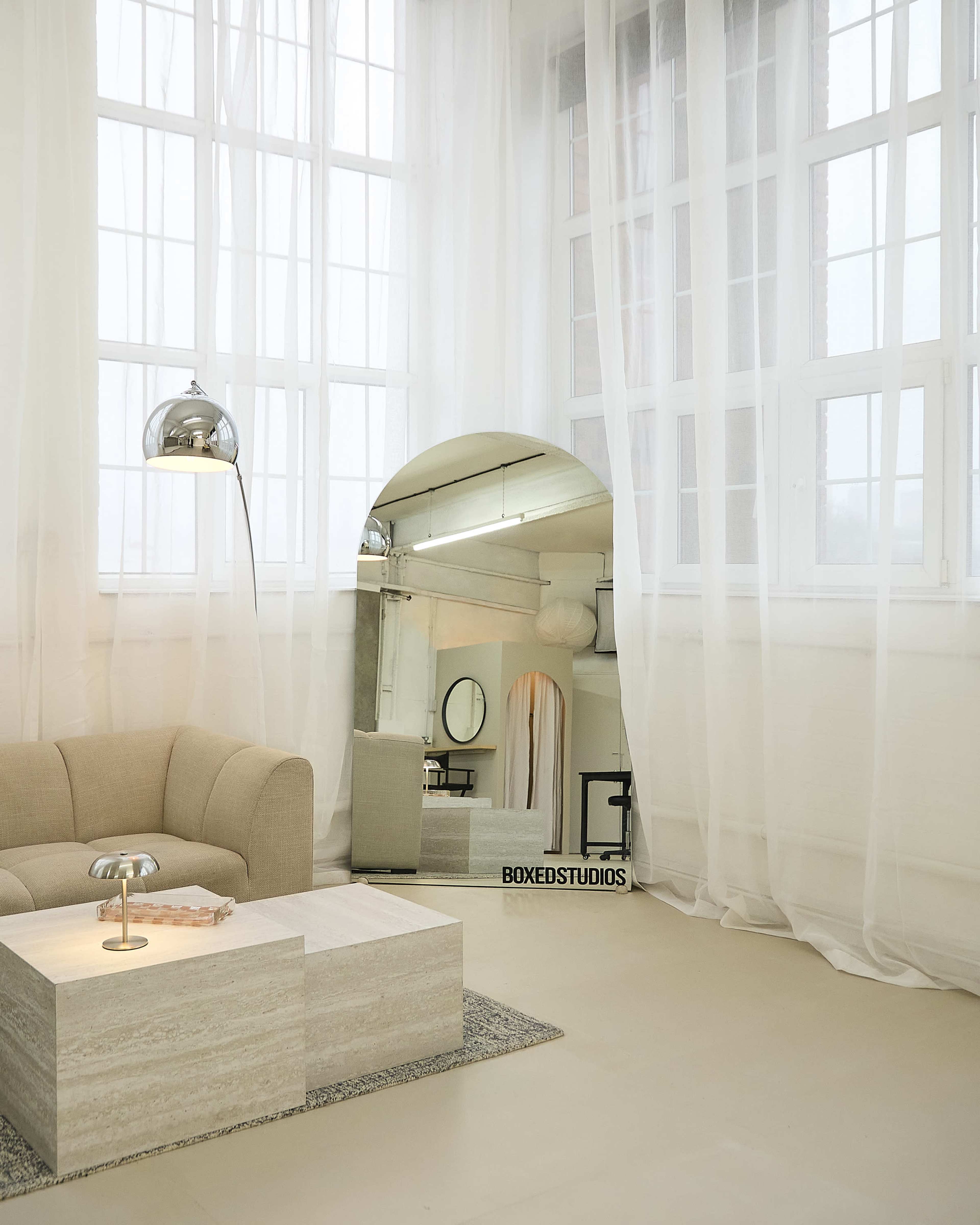 A light-filled room features a beige sofa, a sleek coffee table, and large windows framed by sheer curtains.