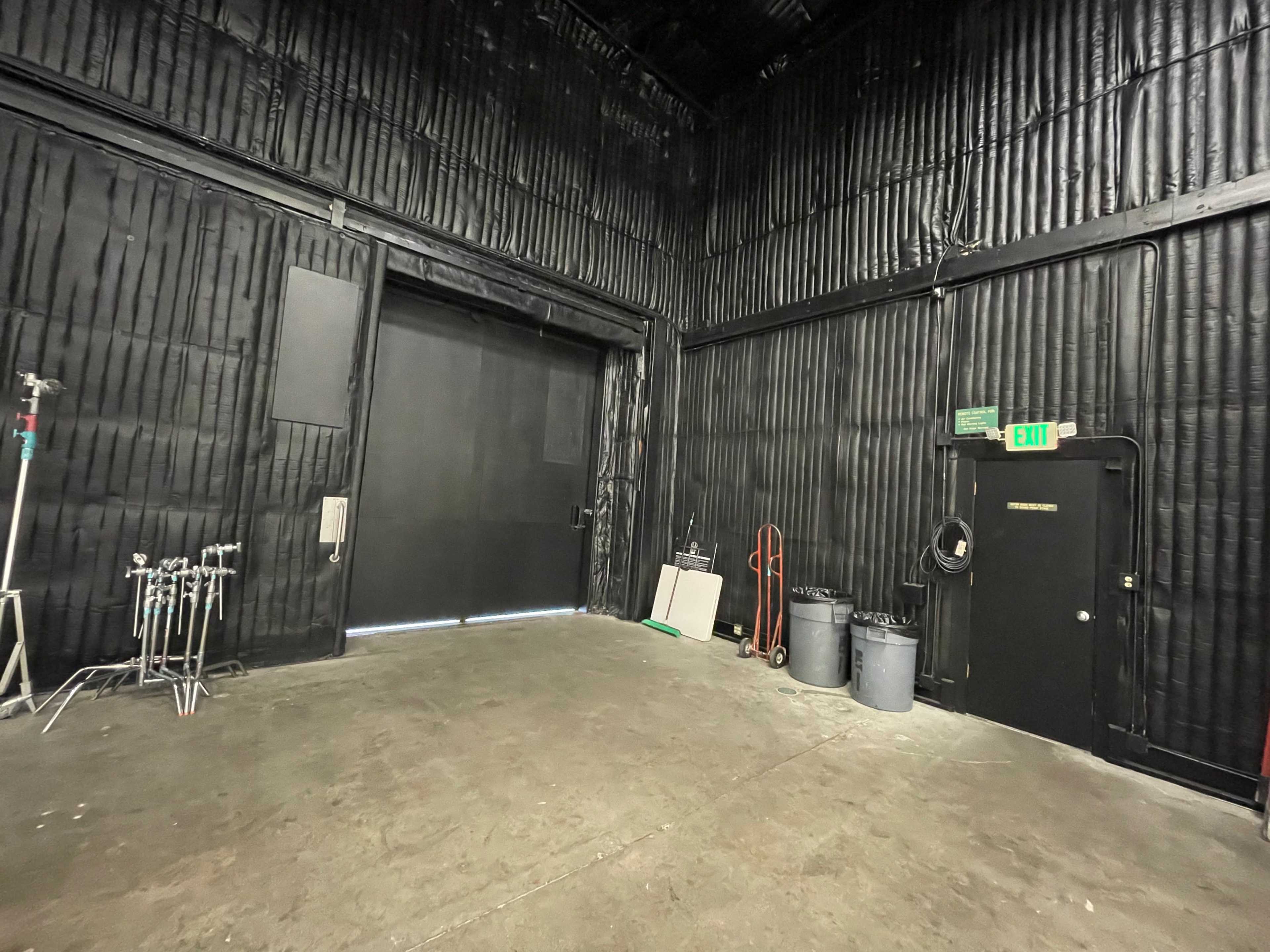 The image shows a dimly lit industrial space with a large black door on one side and various equipment and trash bins along the walls.