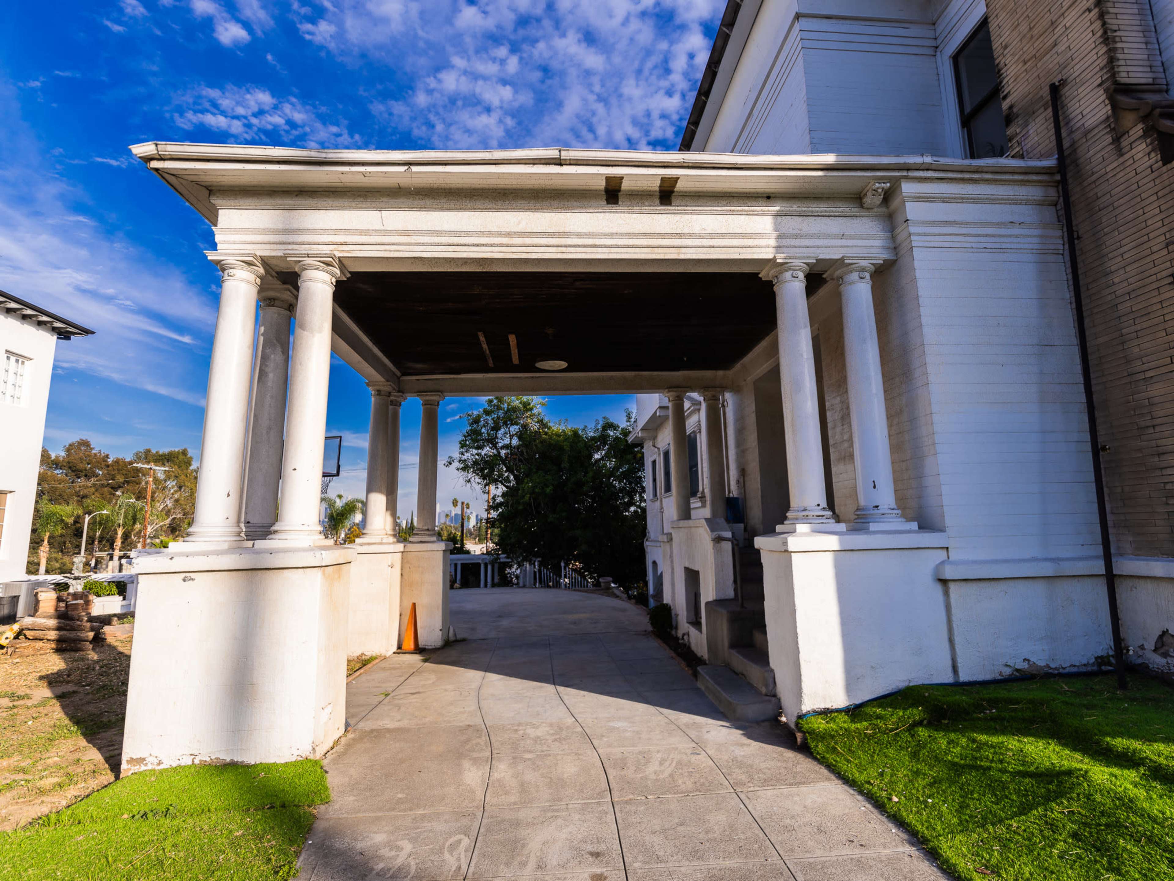 A large entrance with classical columns leading to a building, set against a backdrop of a blue sky with scattered clouds.