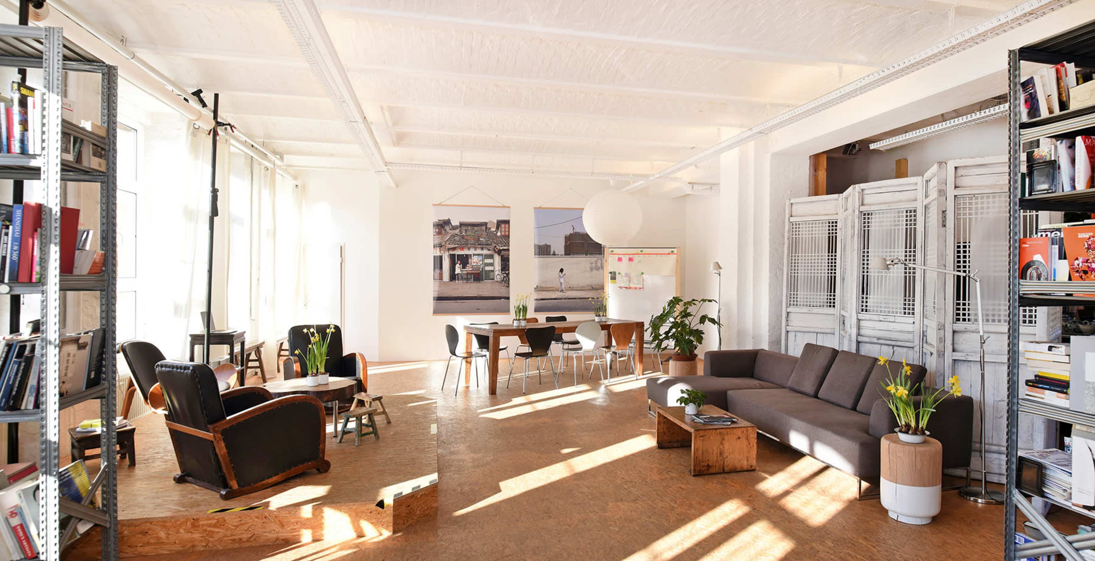A bright, airy room with a mix of seating options, a dining area, and bookshelves filled with books, along with decorative plants and artwork on the walls.