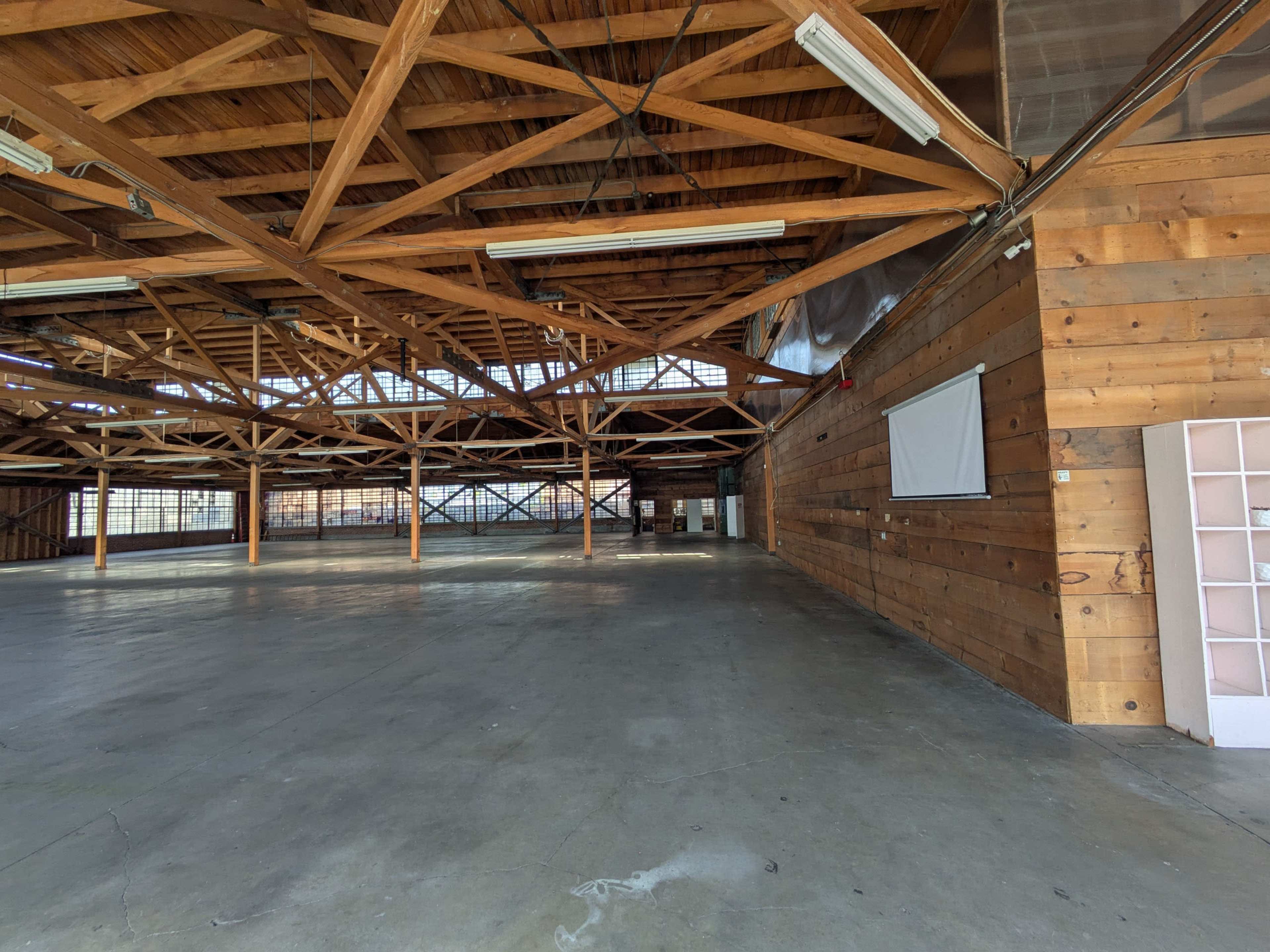 The image shows a spacious, empty interior of a building with exposed wooden beams and large windows.