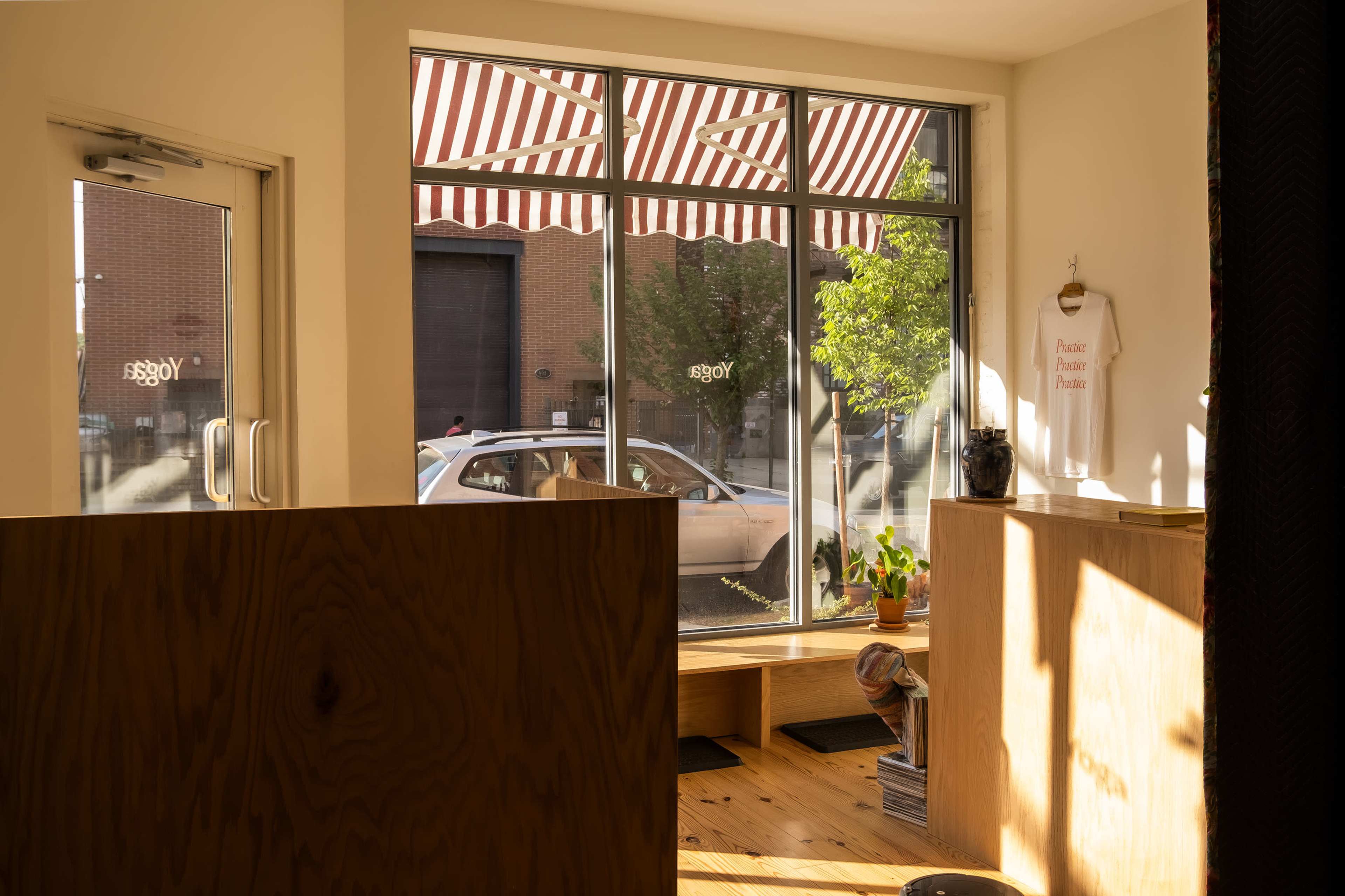 The interior of a shop with wooden counters and large windows featuring striped awnings, allowing sunlight to illuminate the space.
