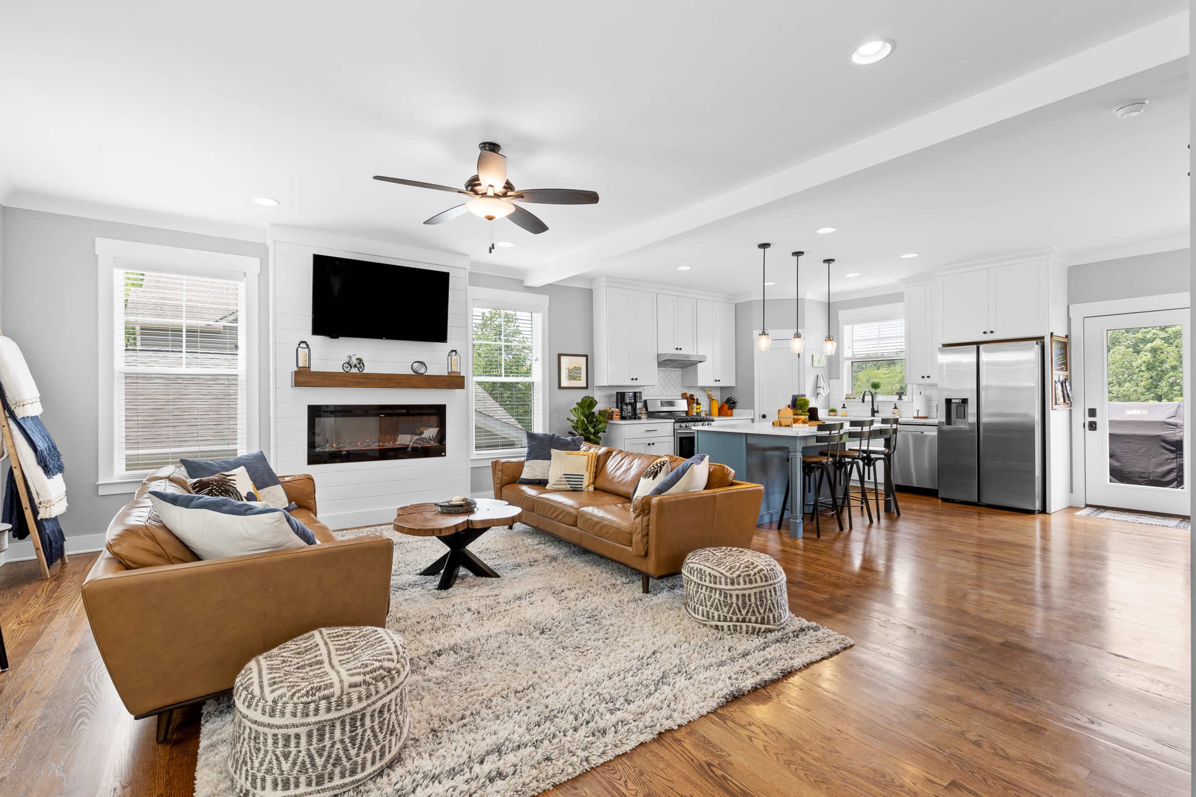 A modern living room and kitchen area, featuring a brown leather sofa, a large rug, and a kitchen island with bar stools.