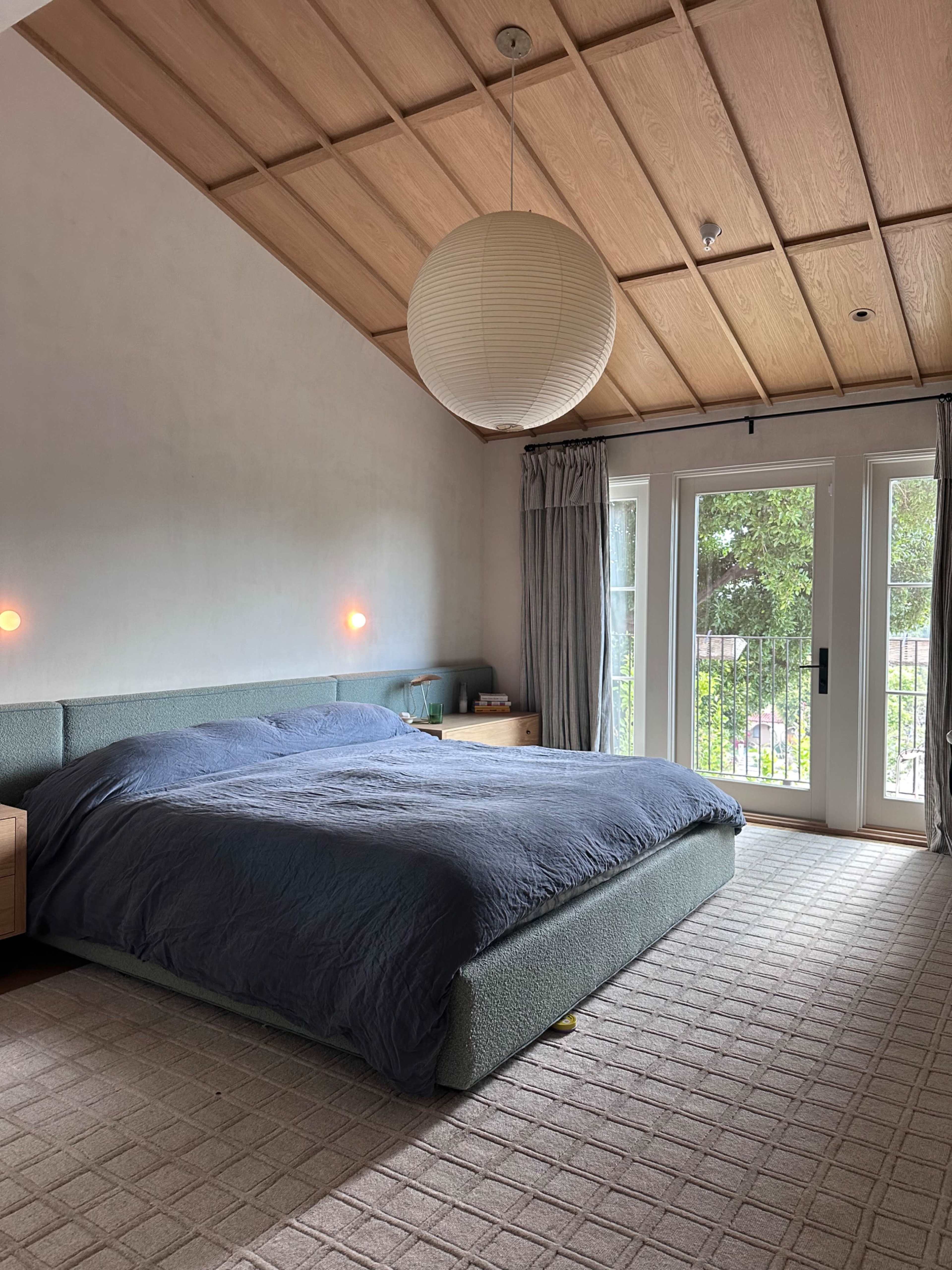 A modern bedroom with a large bed, wooden ceiling, and door leading to an outdoor area.