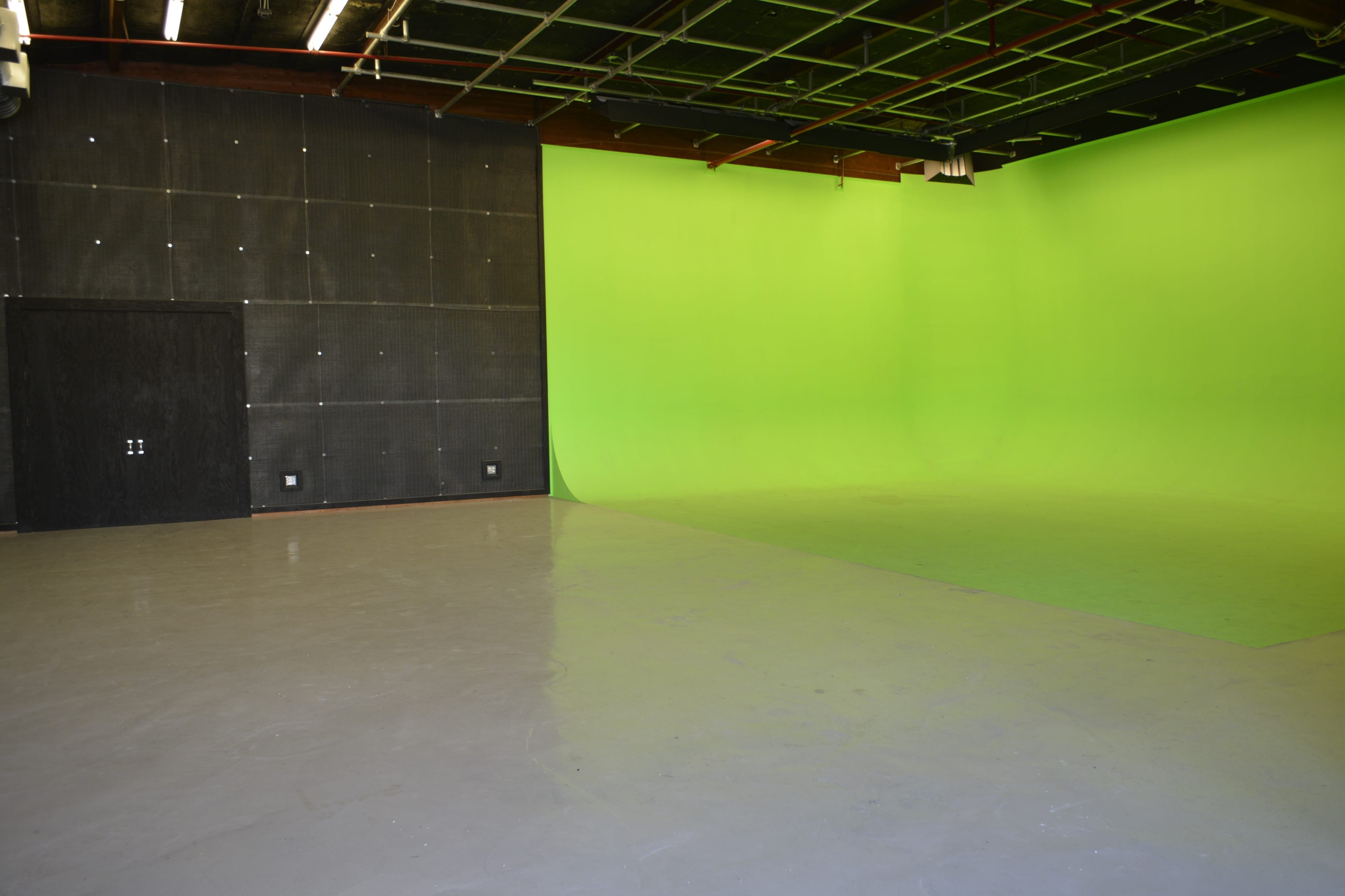 A spacious room featuring a black wall, a green backdrop, and a polished gray floor.