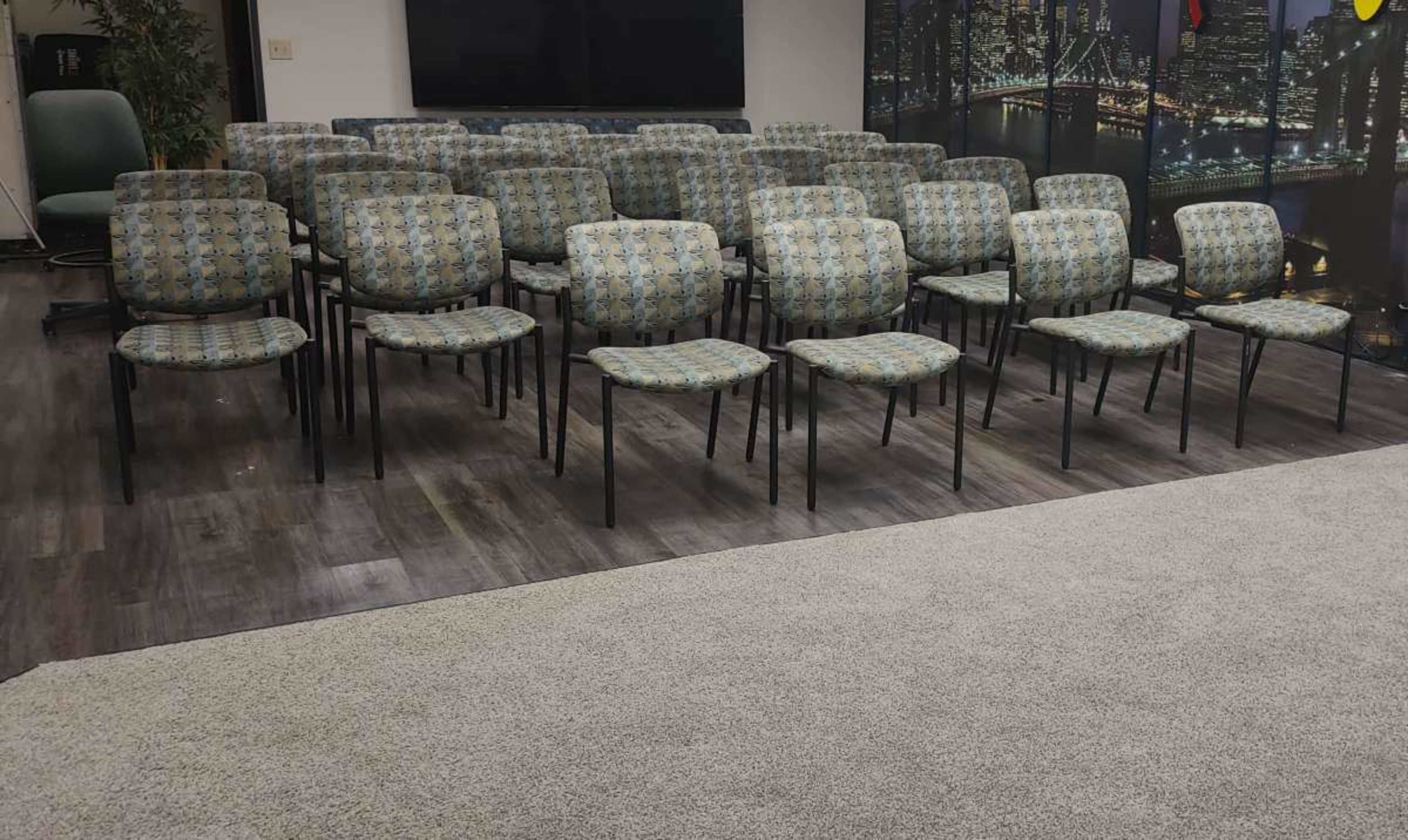 A row of patterned chairs arranged in a meeting room with a dark wall in the background.