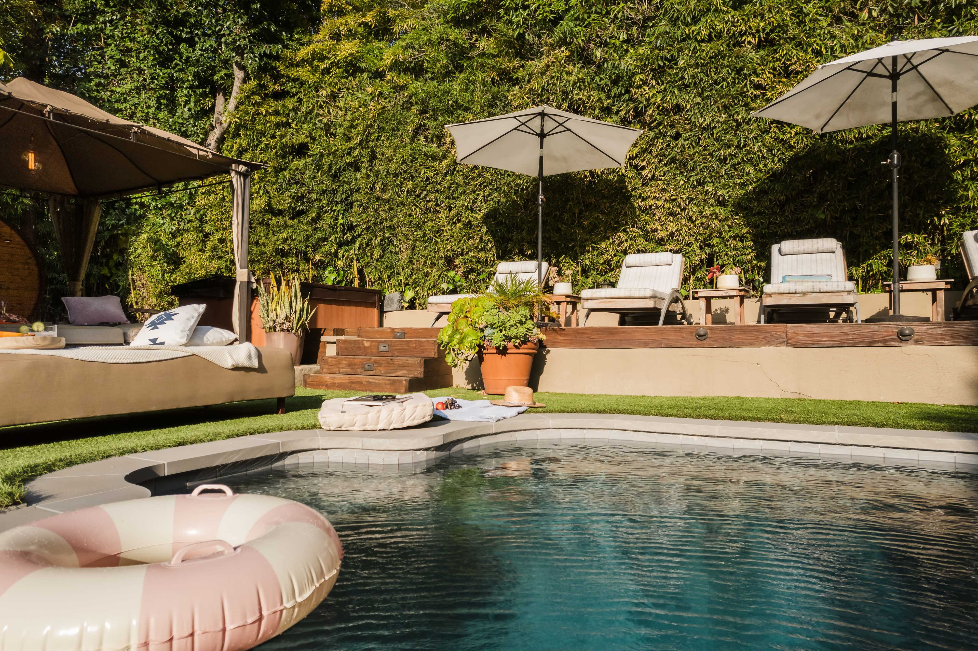 A swimming pool surrounded by lounge chairs, umbrellas, and a gazebo, with a cozy area for relaxation and lush greenery in the background.