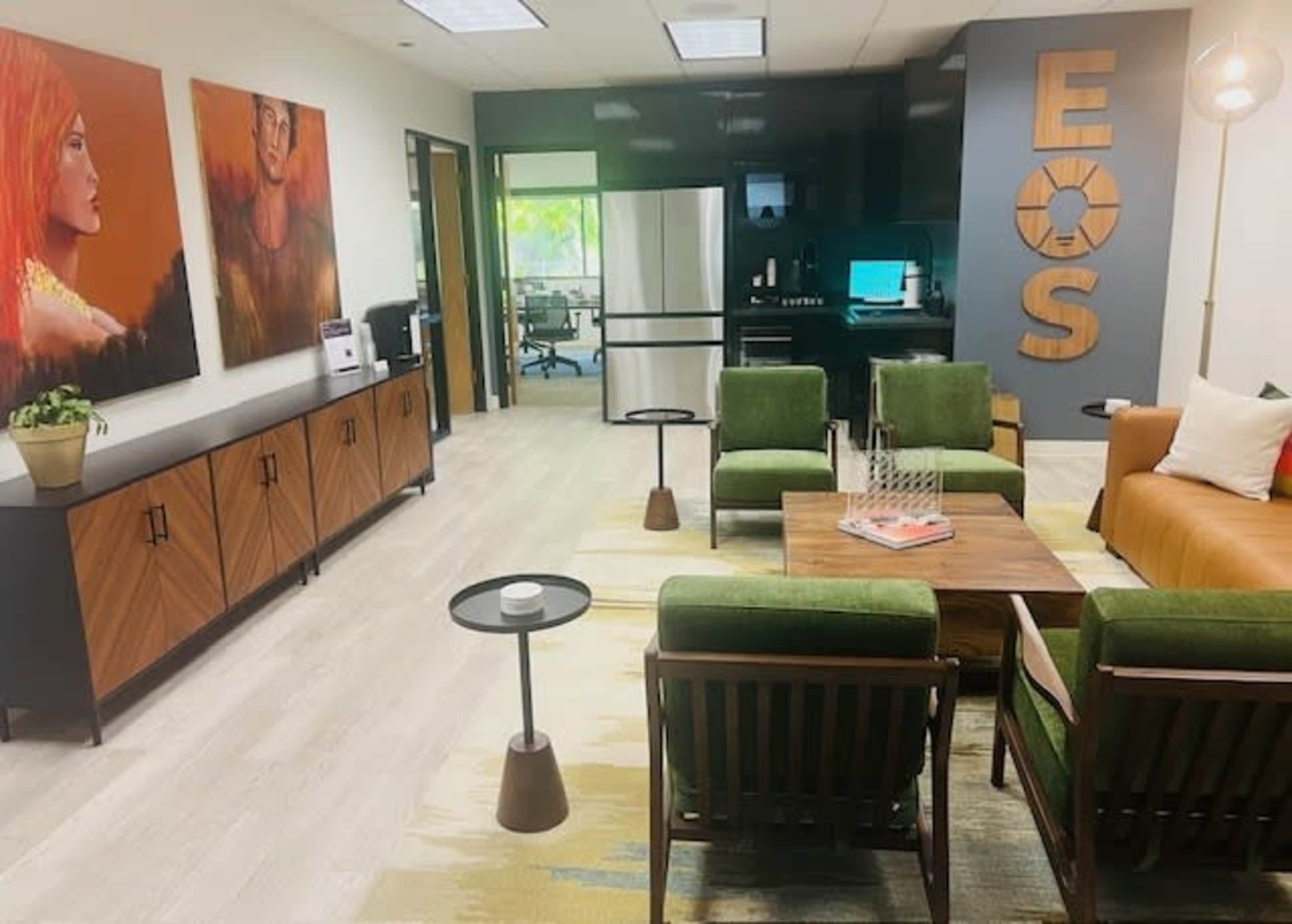 A modern office space featuring a seating area with green chairs, a brown couch, and two large paintings on the wall.