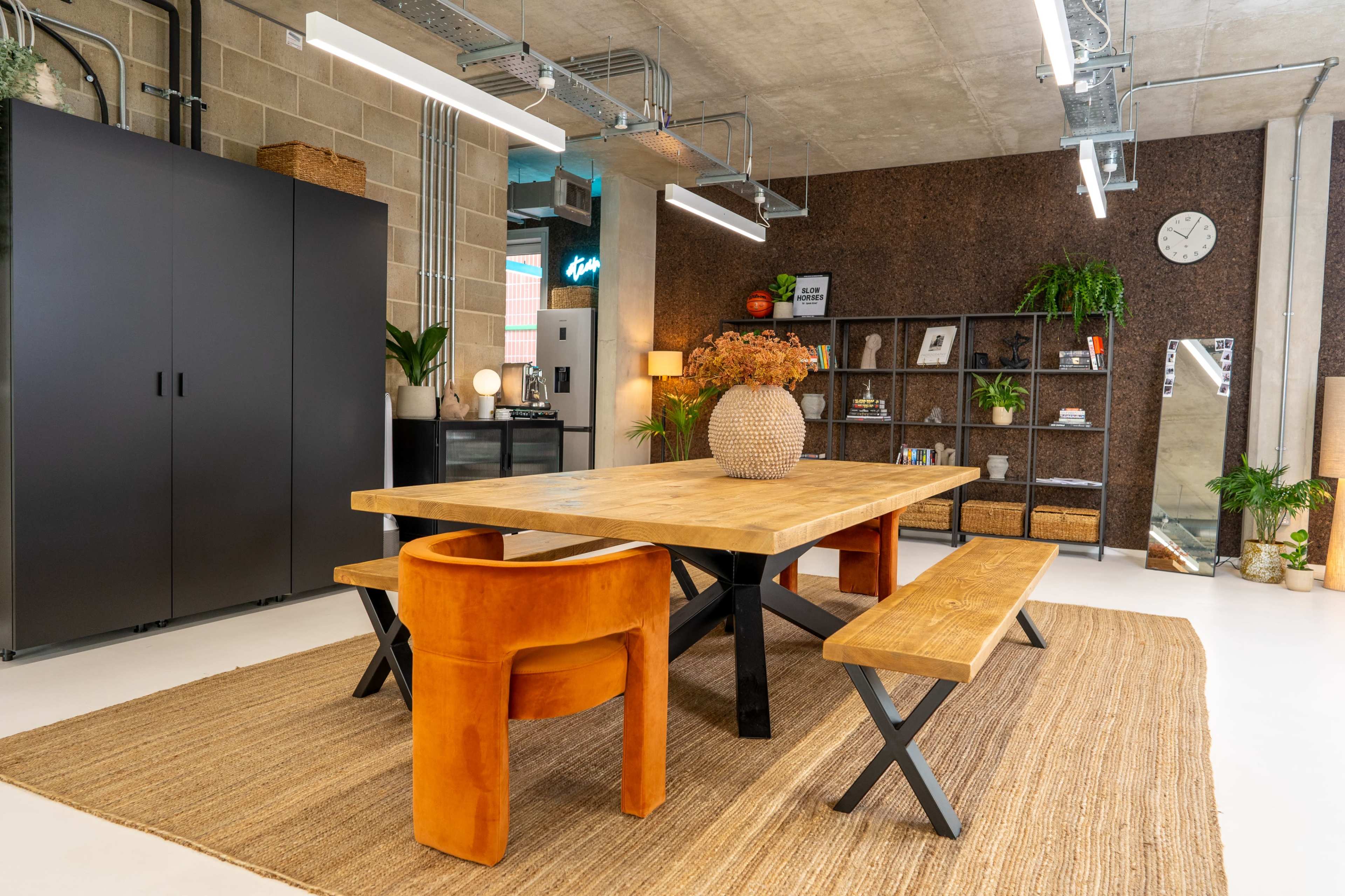 The image shows a modern dining area featuring a wooden table with benches, a round vase, and black storage cabinets against a textured wall.