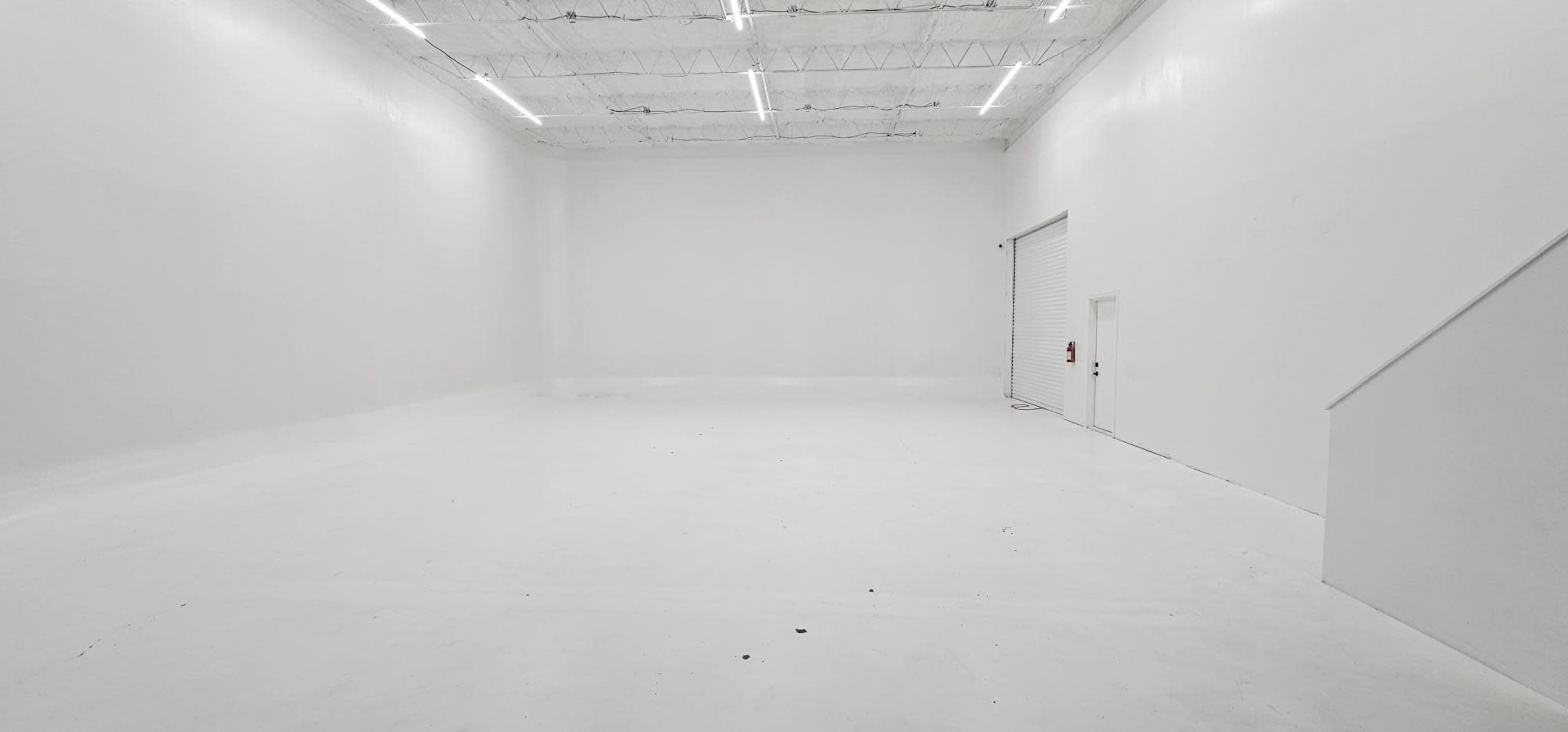 A large, empty white room with high ceilings and a door on one side.