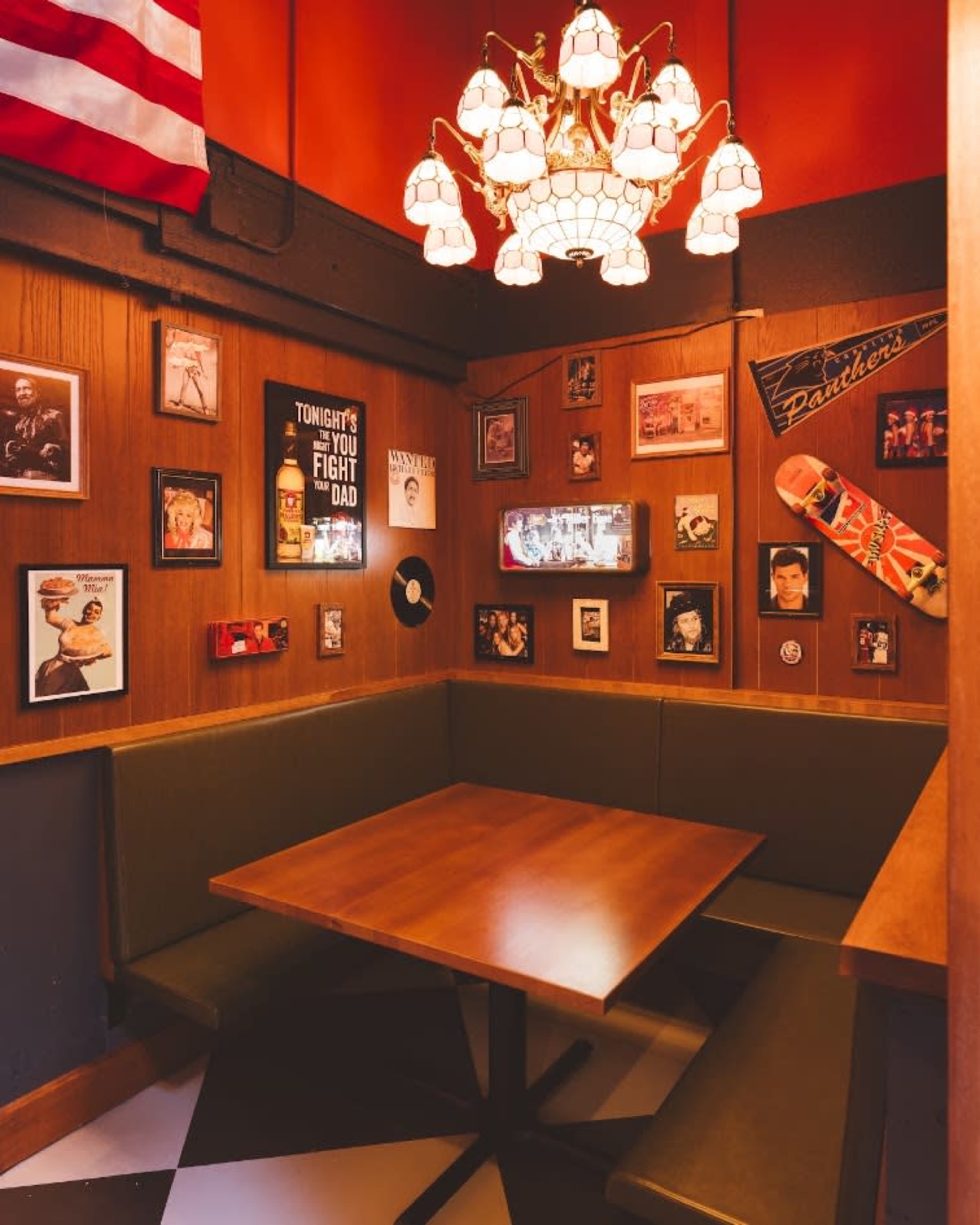 A cozy booth in a restaurant features a wooden table surrounded by a wall adorned with framed photographs and decorative items, including a chandelier overhead.