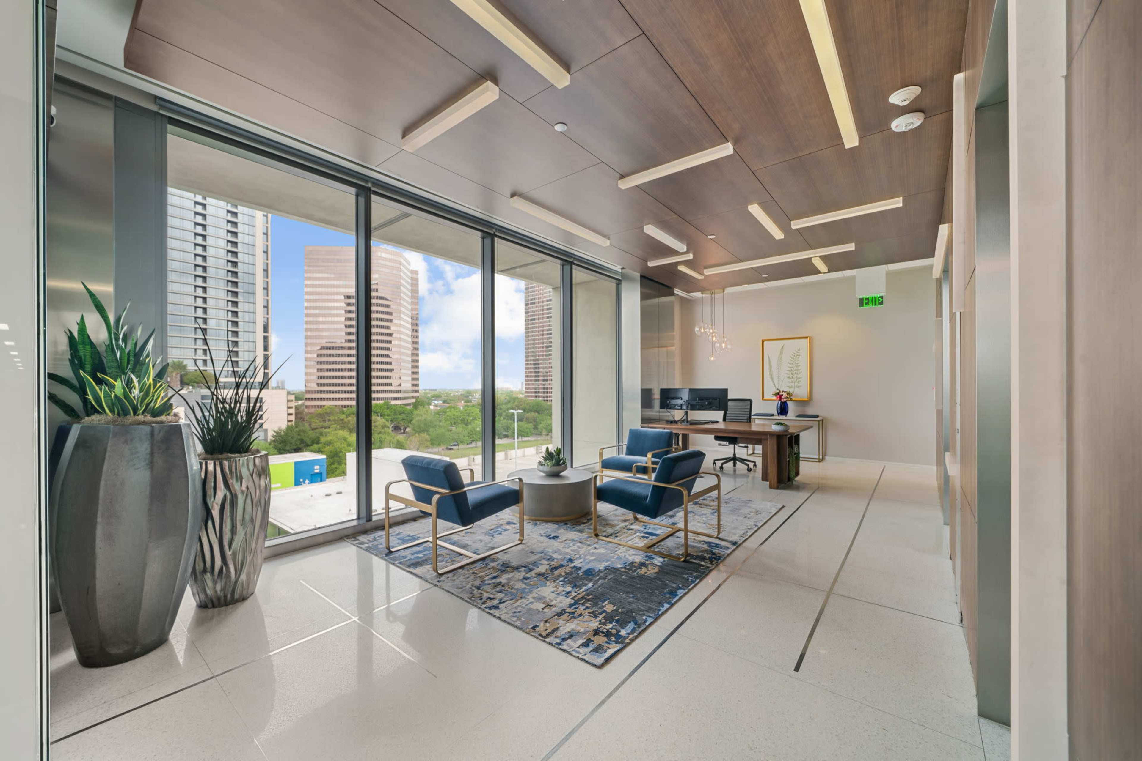 A modern office space features large windows, contemporary furniture, and decorative plants.