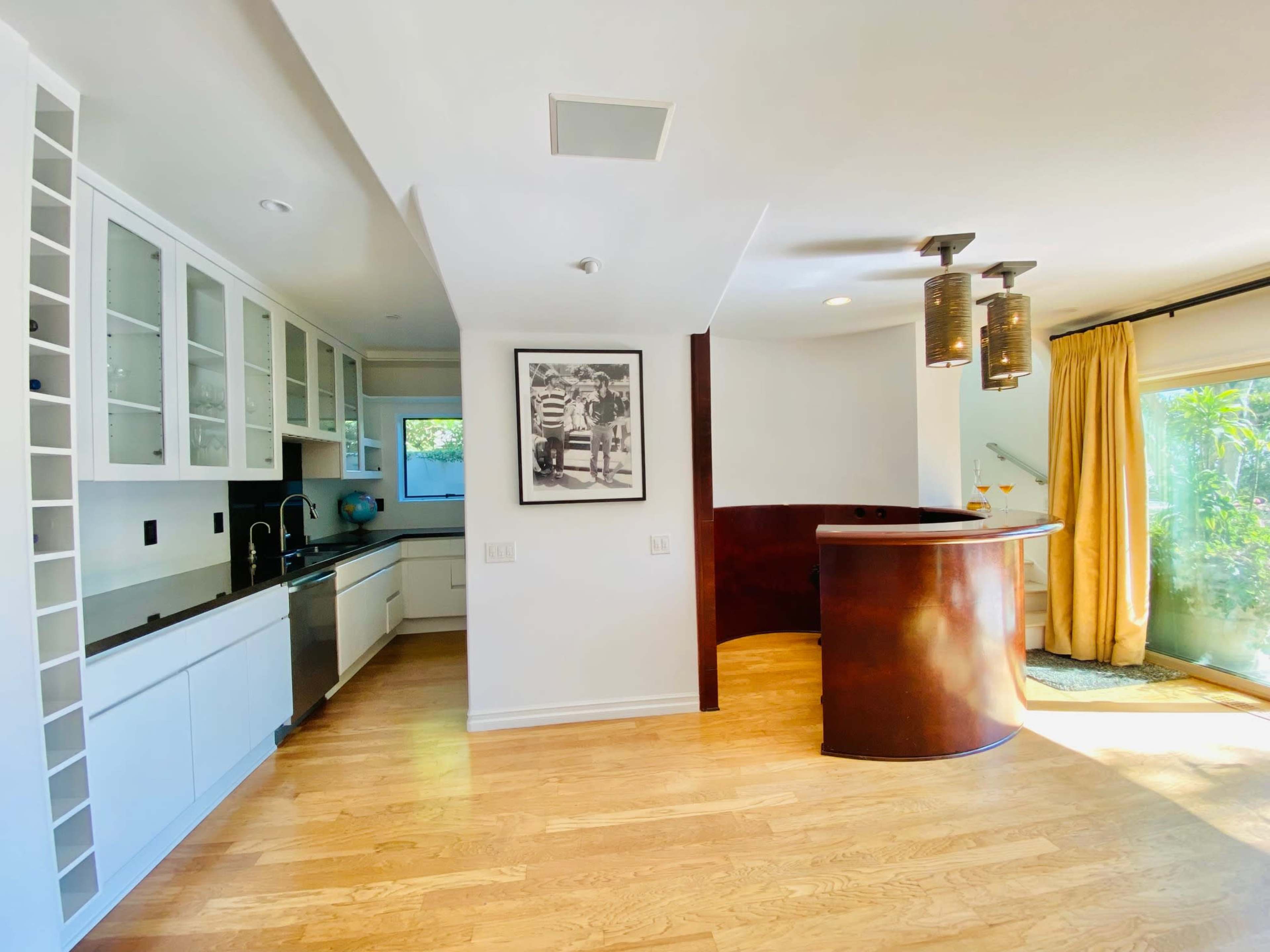 A modern kitchen and bar area with white cabinetry, black countertops, and large windows that let in natural light.