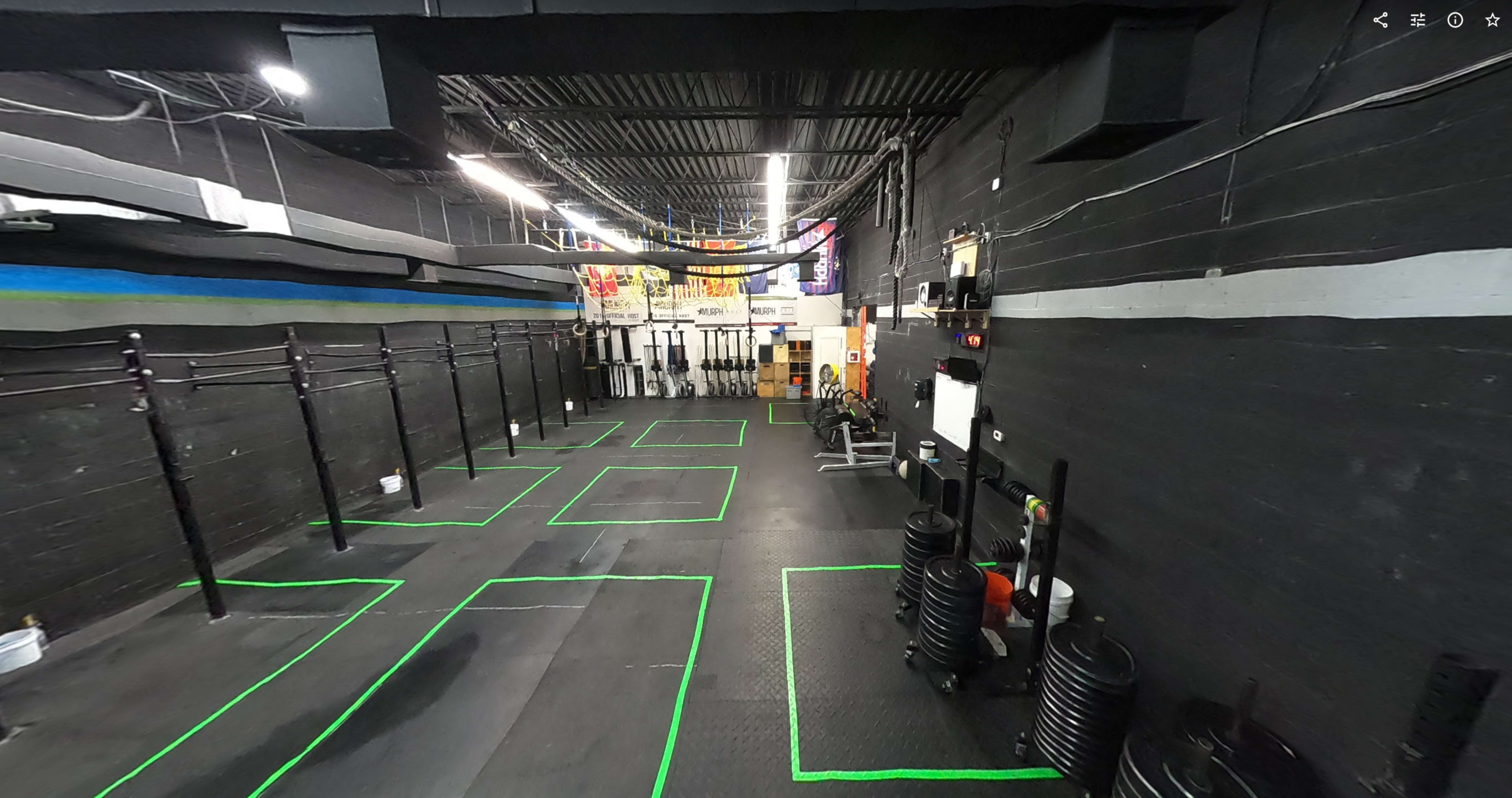 An organized gym interior with marked workout areas, racks for weights, and various exercise equipment along the walls.