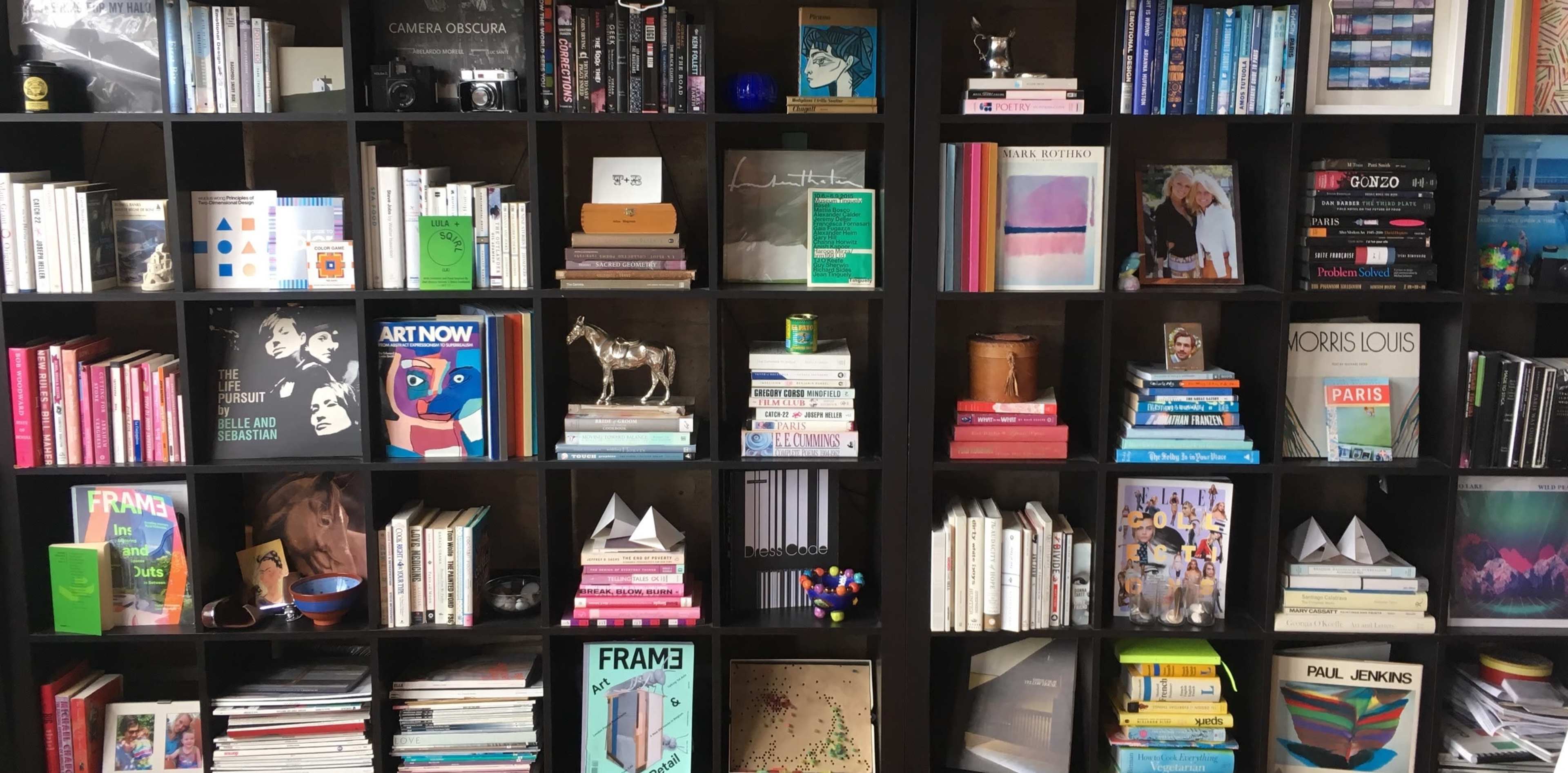 A bookshelf filled with various books, magazines, decorative items, and photography equipment organized neatly across multiple shelves.