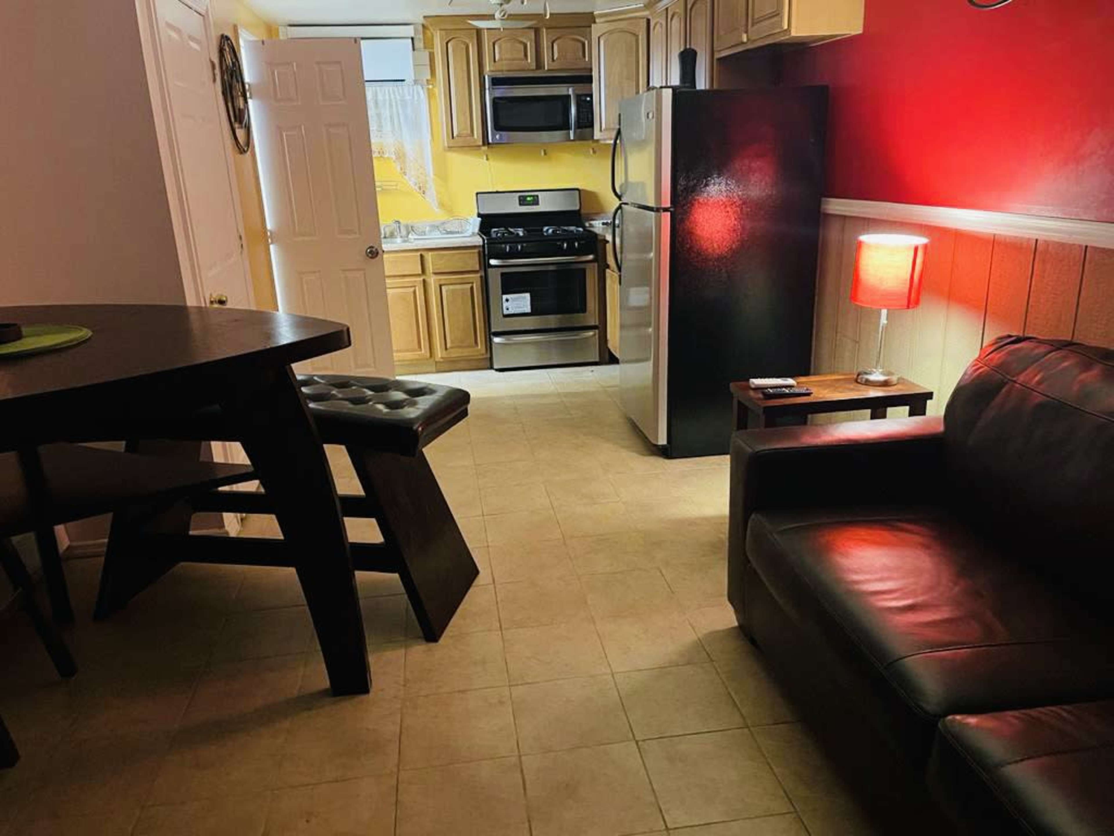 A small kitchen and living area featuring a black sofa, a round dining table, and kitchen appliances against a red and beige wall.