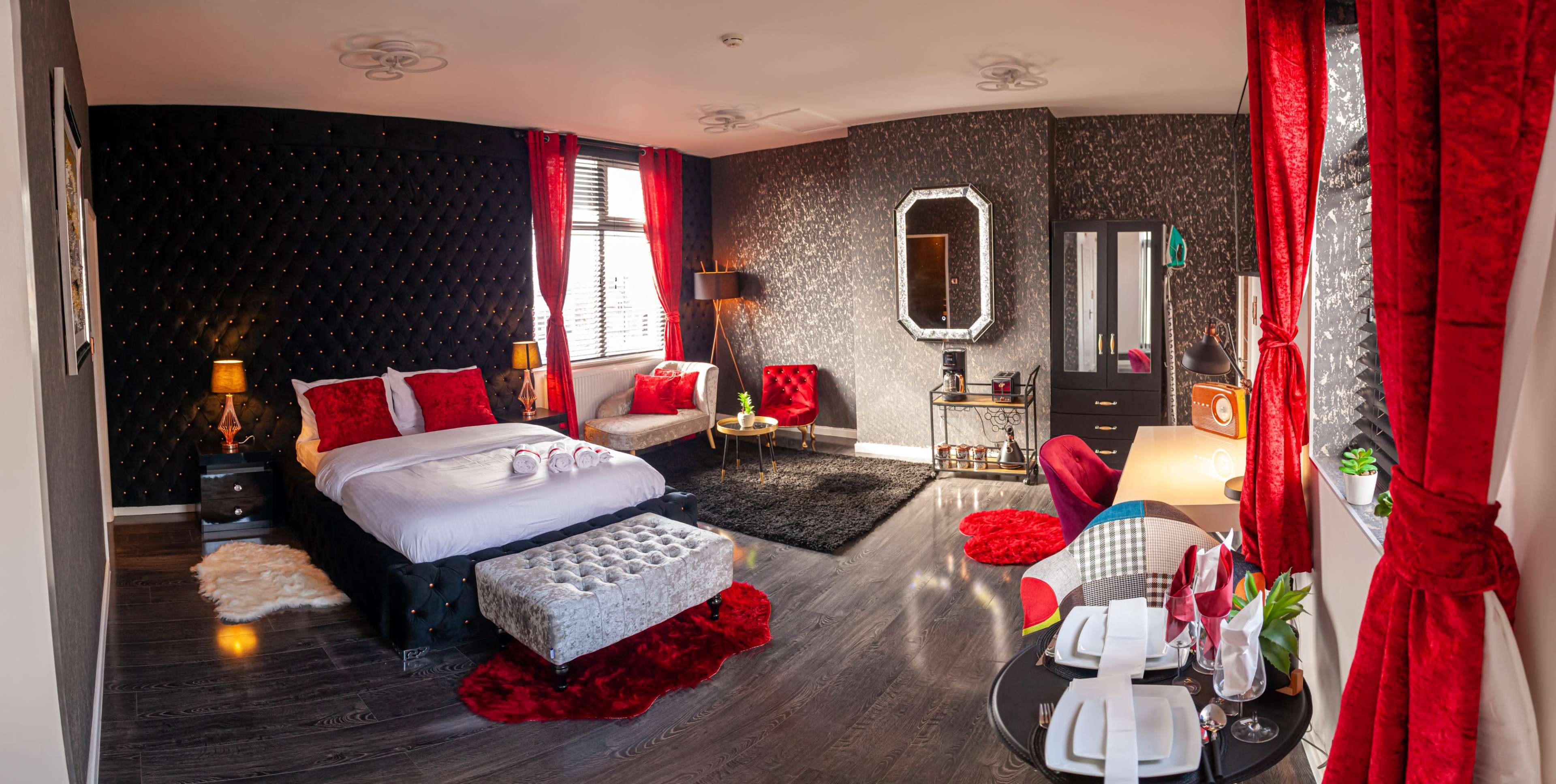 A modern hotel room featuring a bed with white linens, black and red decor, a plush area rug, and a seating area with a round table and chairs.