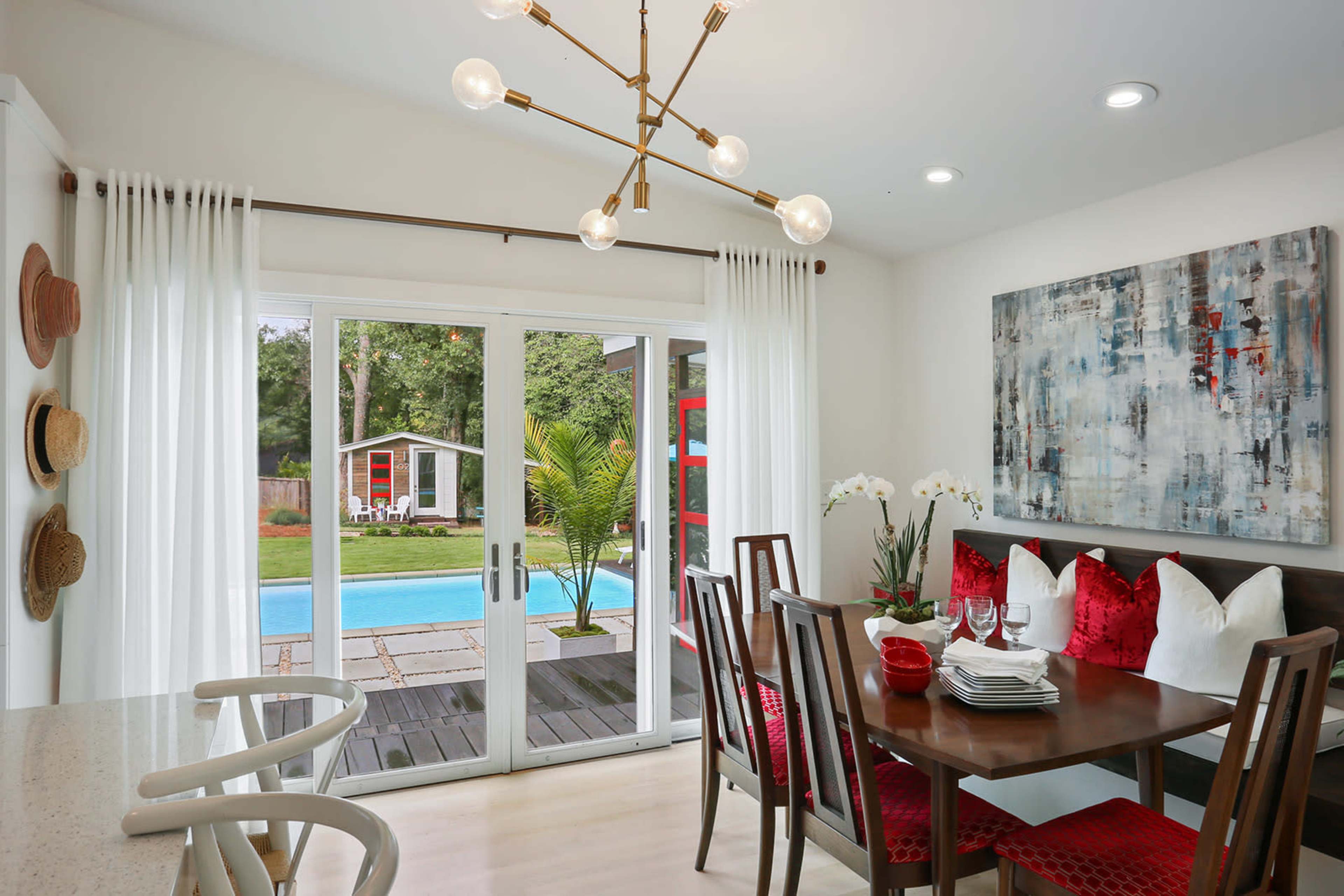 A dining area features a wooden table set for four, surrounded by chairs, with sliding glass doors leading to a patio and pool area.