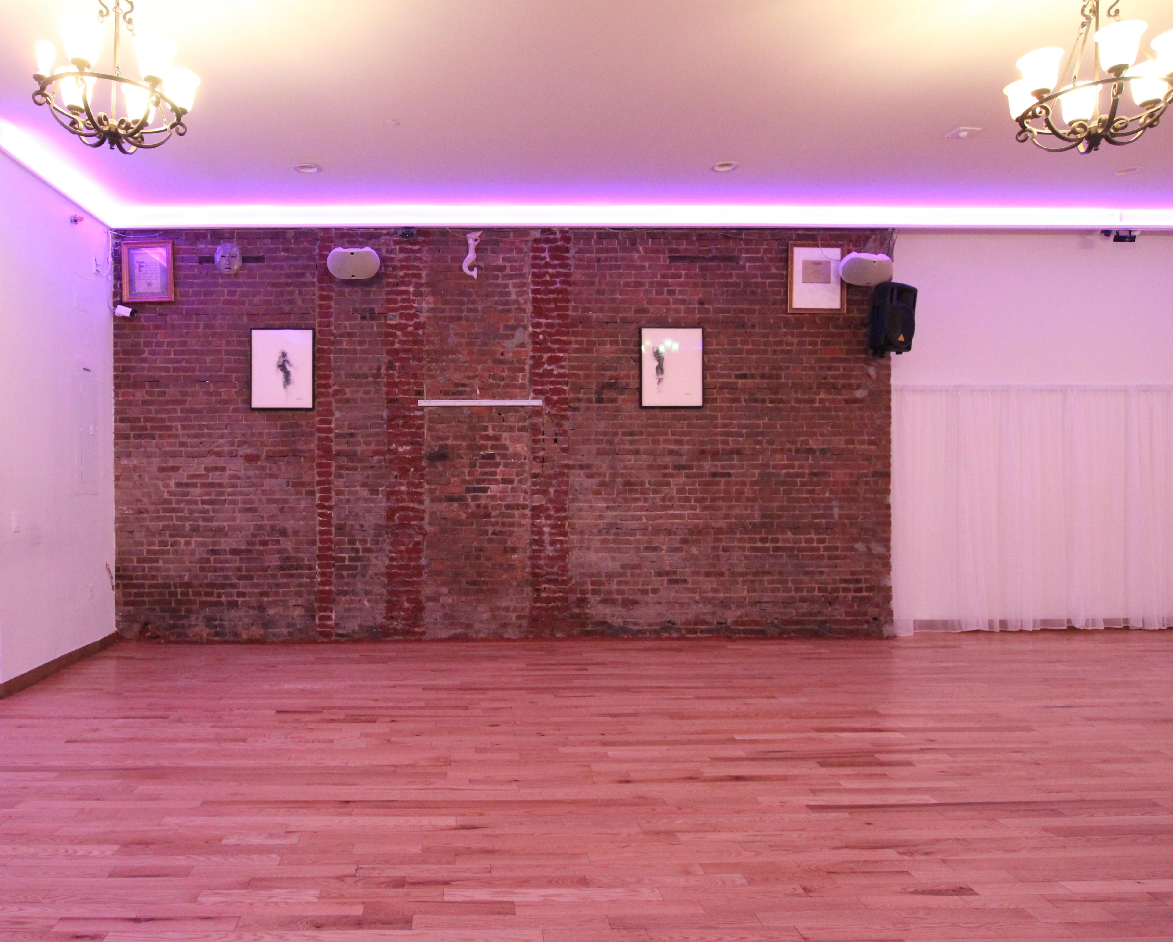 A spacious interior with a brick wall, wooden flooring, and soft lighting from chandeliers and a purple LED strip.