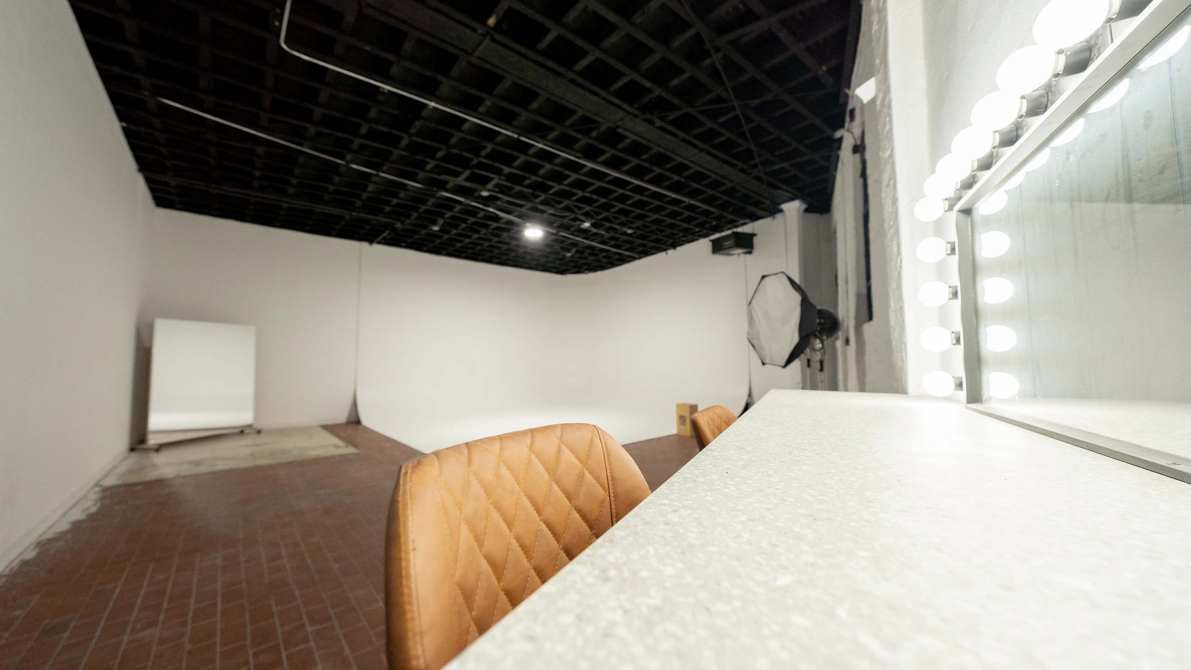 A minimalist studio space with a vanity mirror, a brown chair, and a white backdrop.