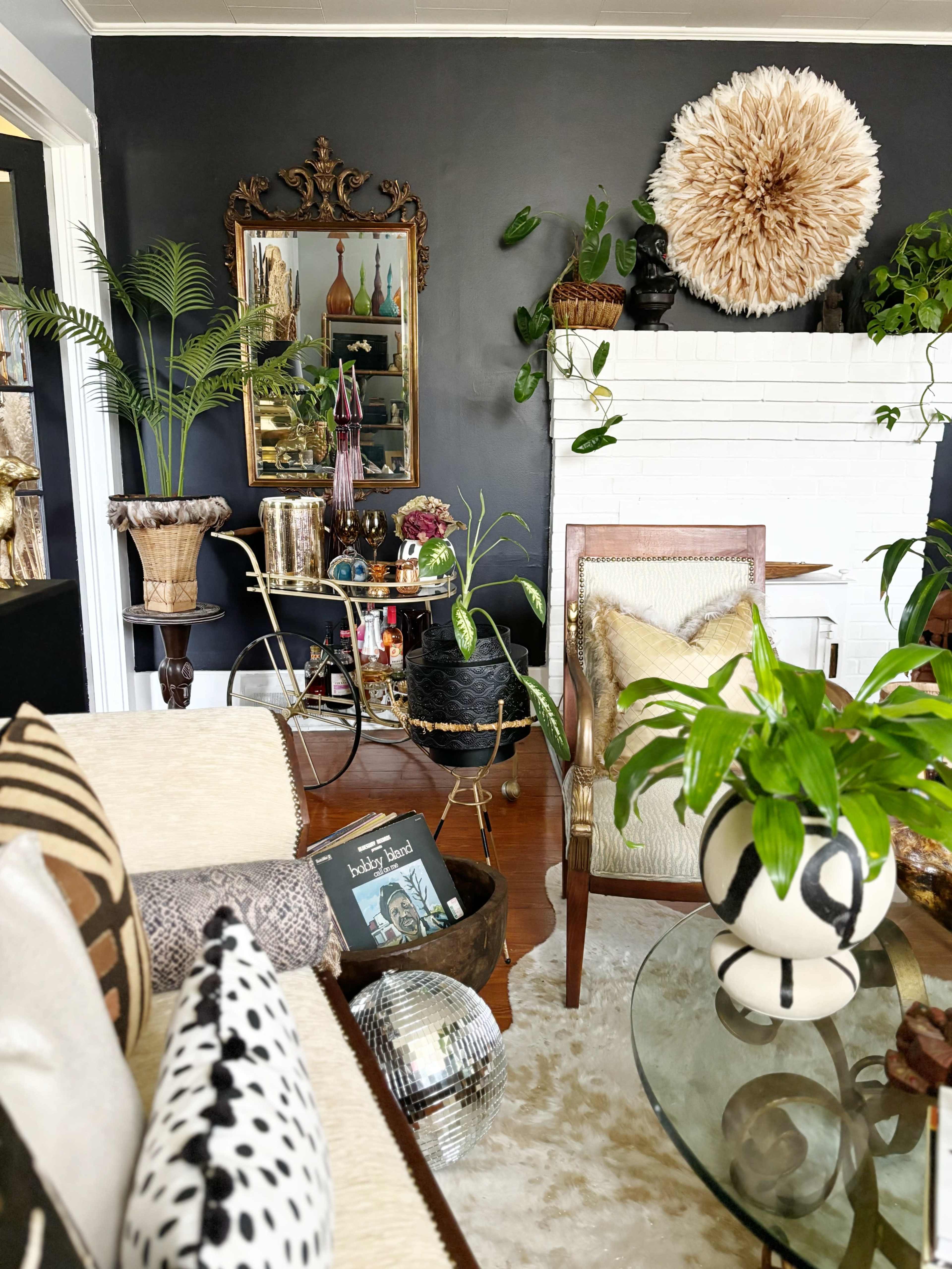 The interior space features a mix of plants, vintage furniture, and decorative elements against a dark wall.