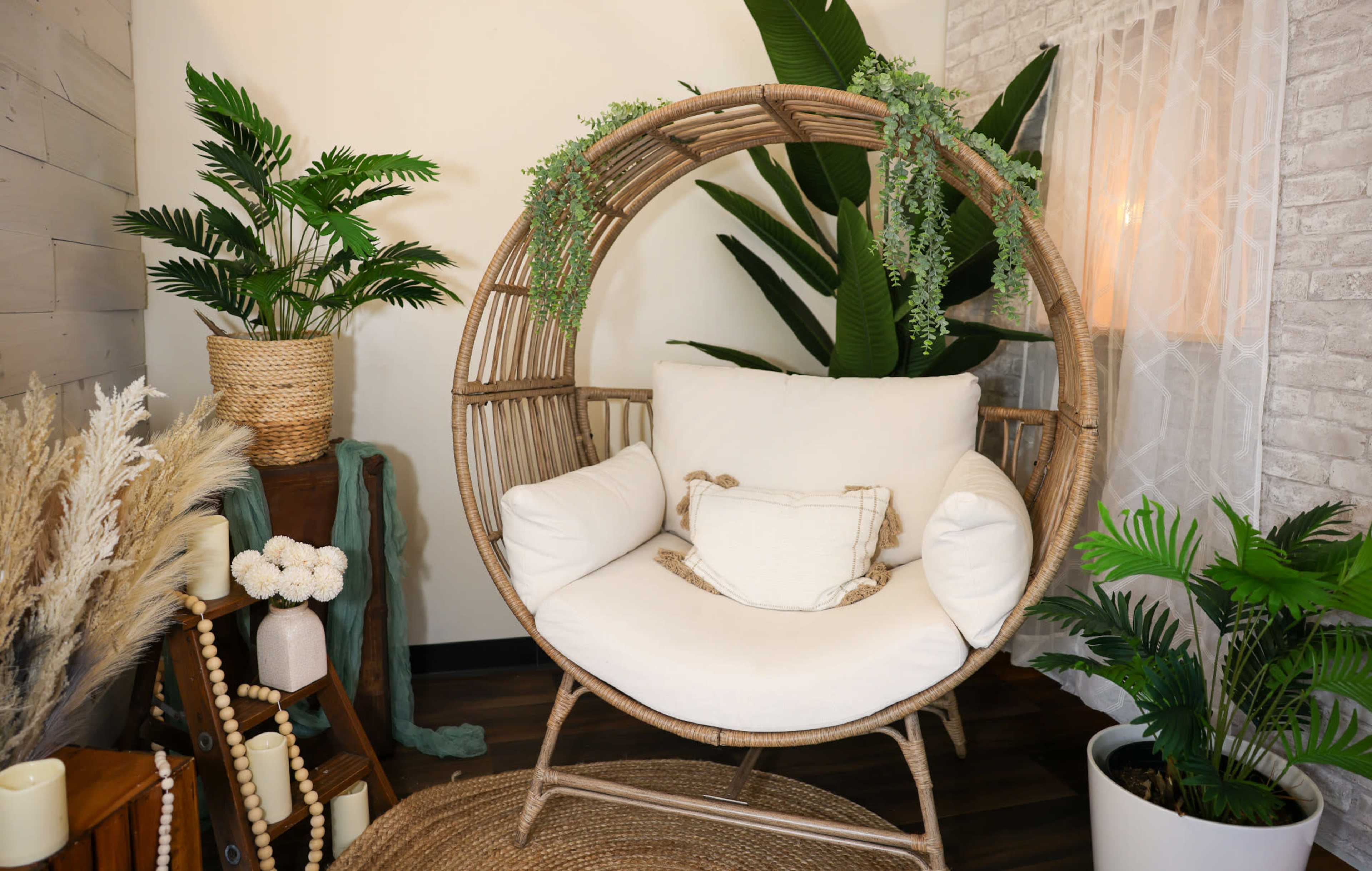 The image shows a circular rattan chair with white cushions, surrounded by indoor plants and decorative elements in a cozy interior setting.