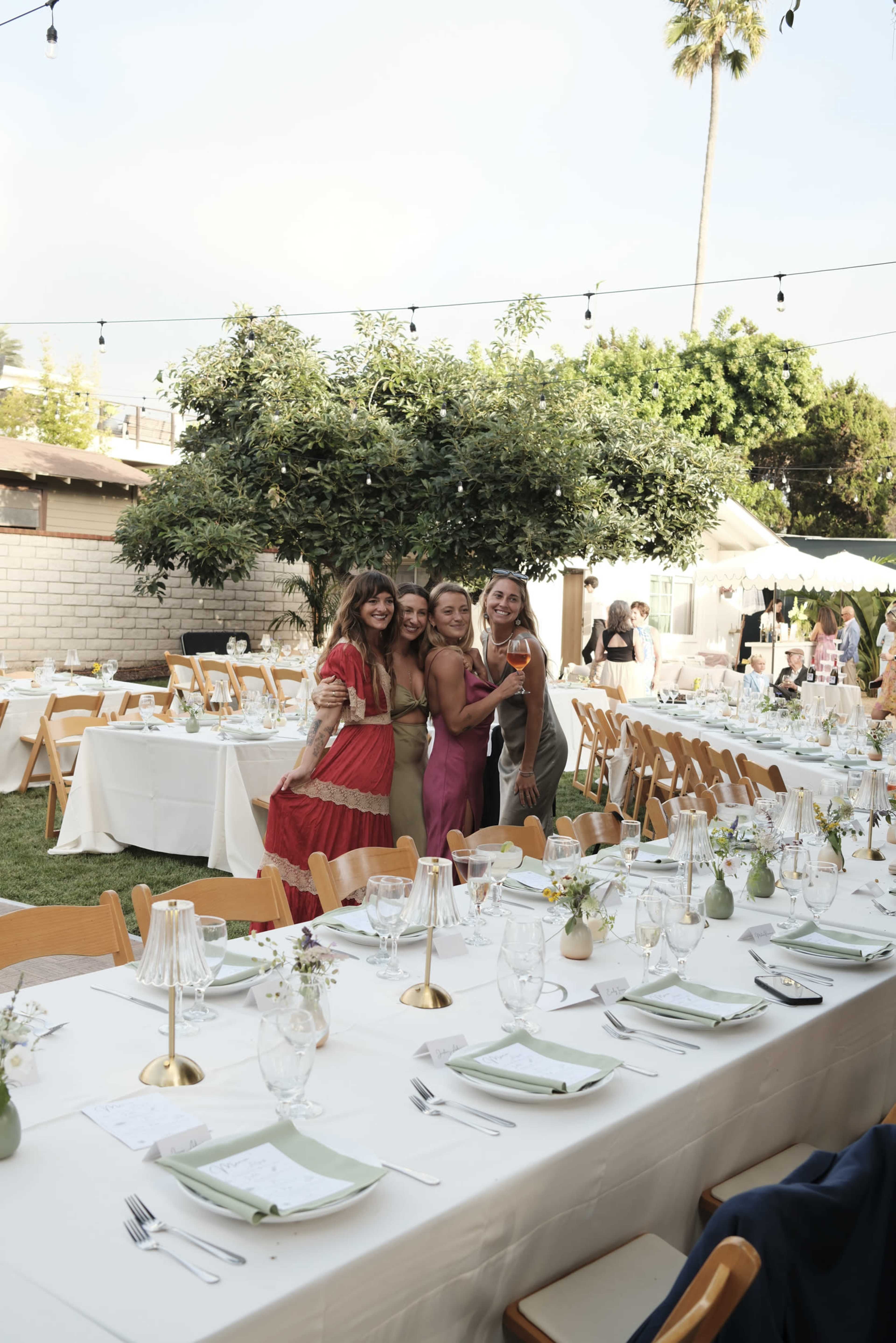 A group of four women pose together in a decorative outdoor dining area adorned with tables set for an event.