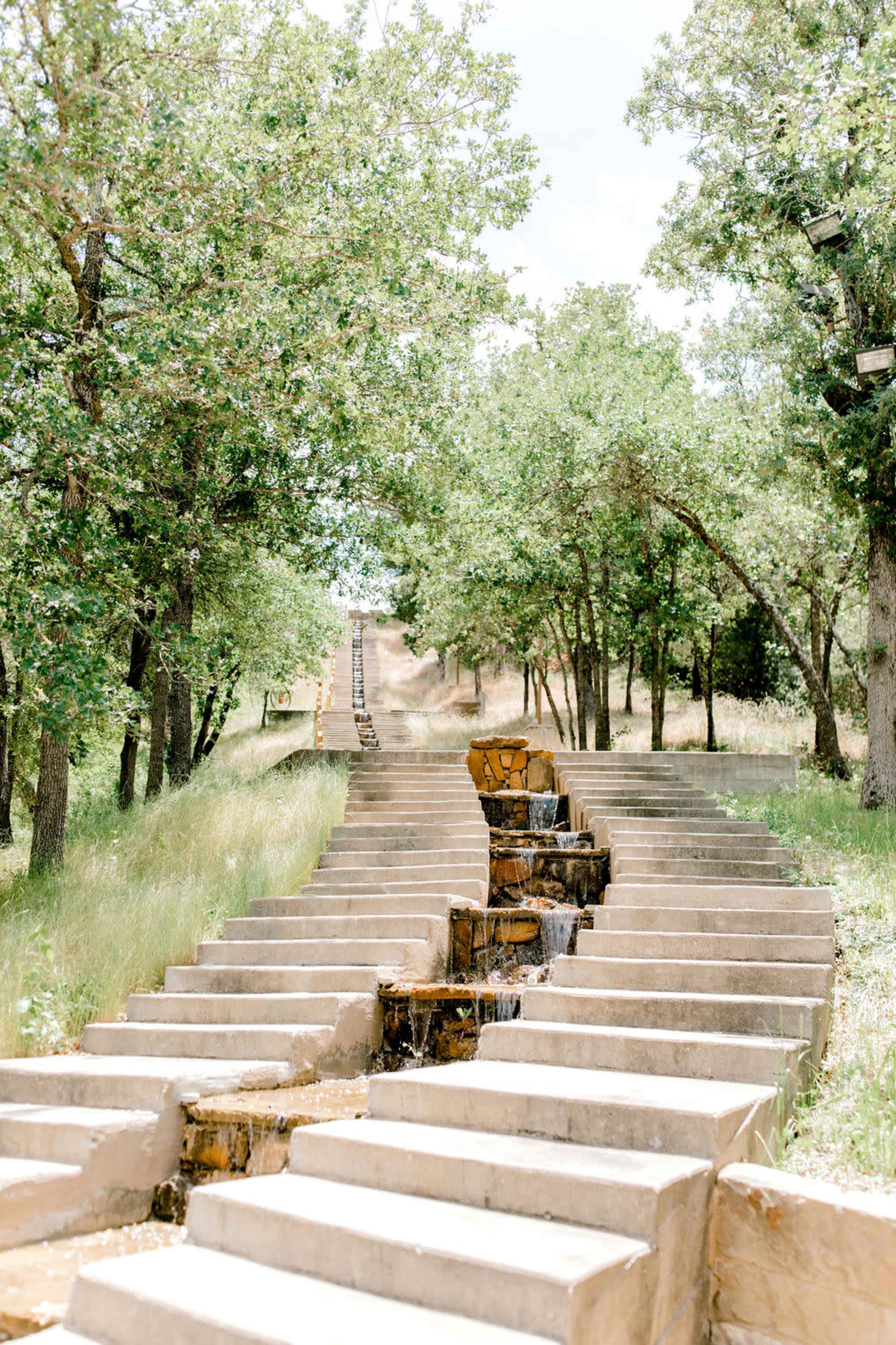 The image shows a stairway with a flowing water feature surrounded by trees and greenery.