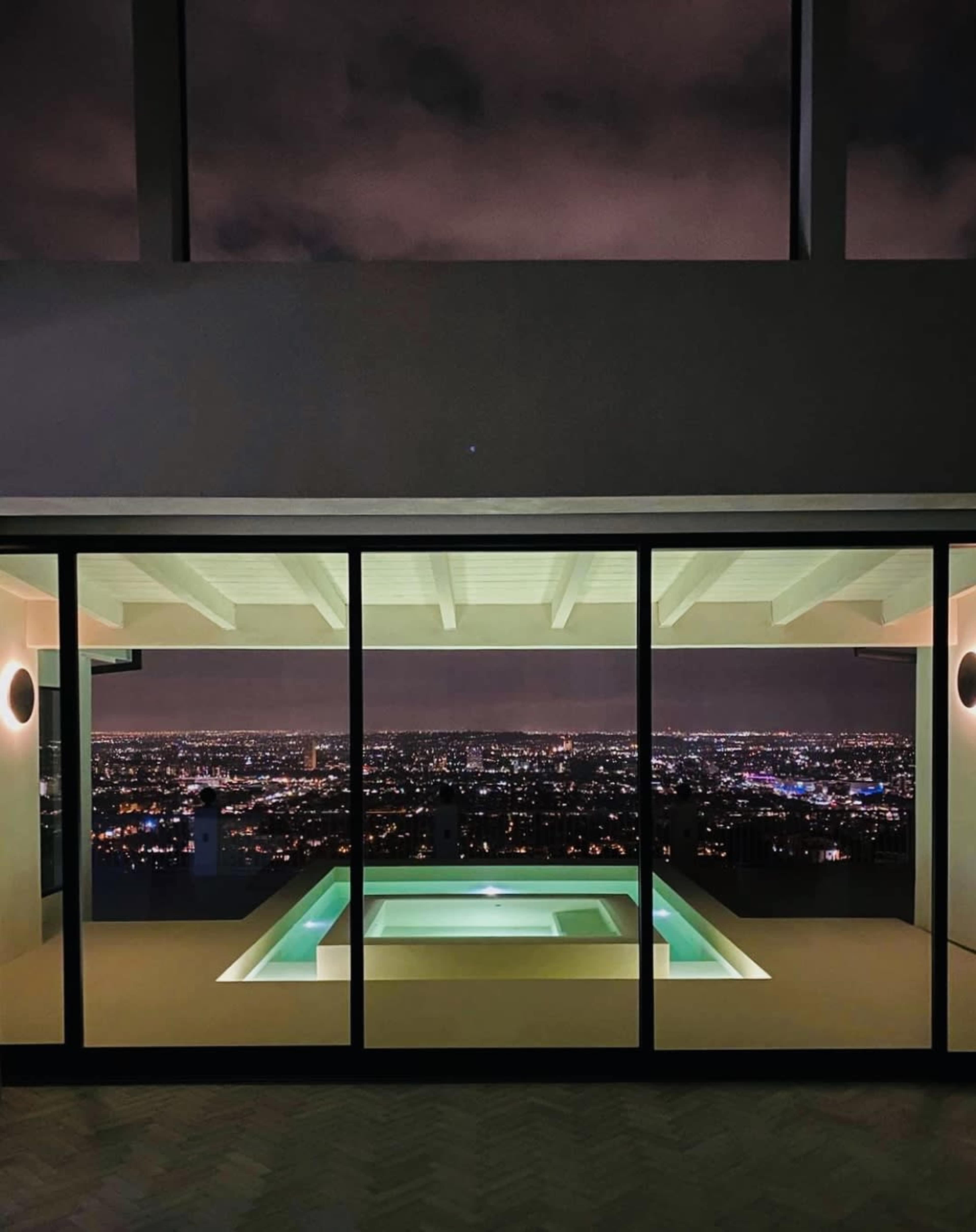 A modern interior with a pool overlooking a city skyline at night, framed by large glass windows.