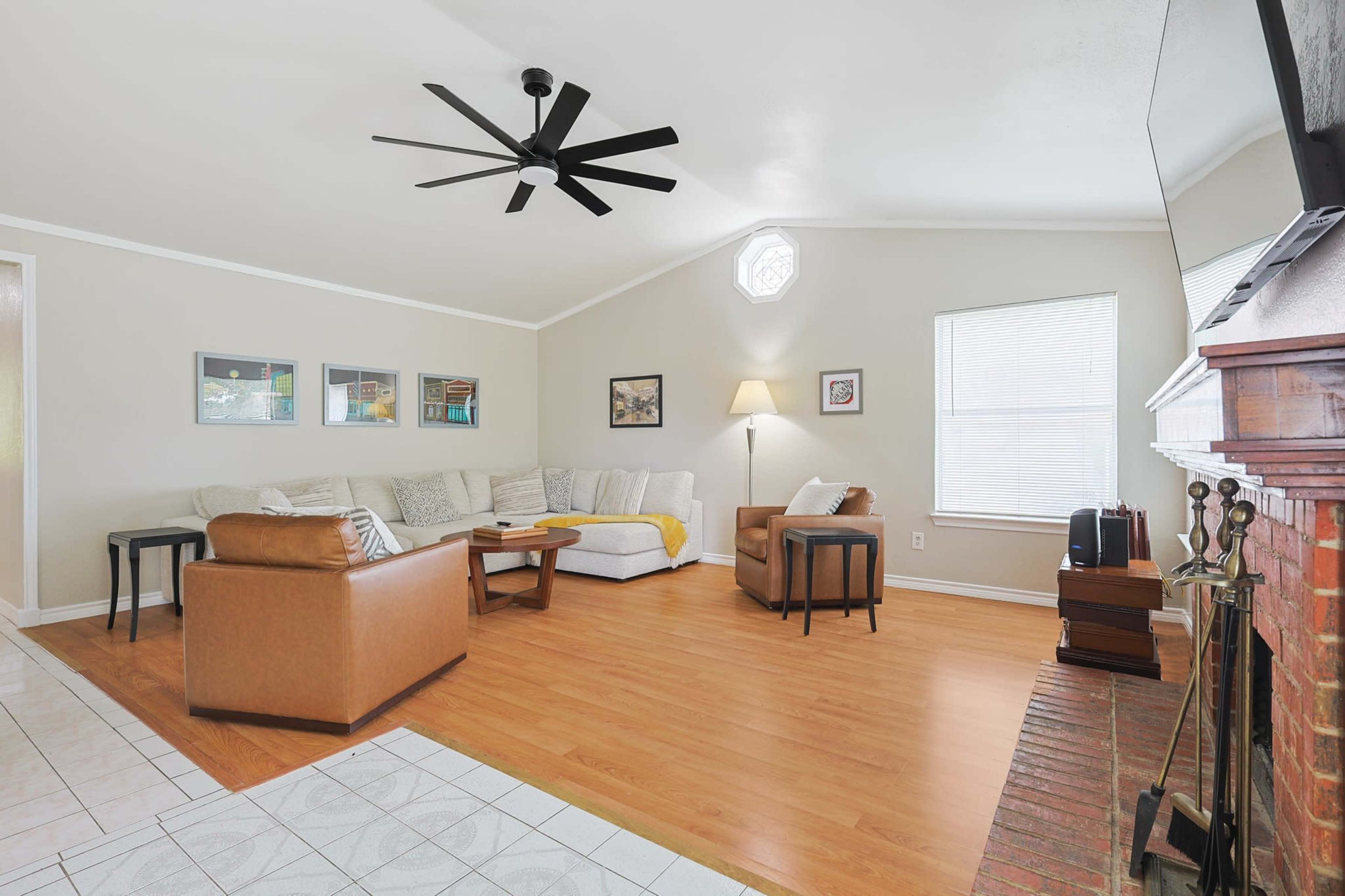 The living room features a sectional sofa, a coffee table, and a seated area with a lamp, set against a backdrop of neutral walls and hardwood flooring.