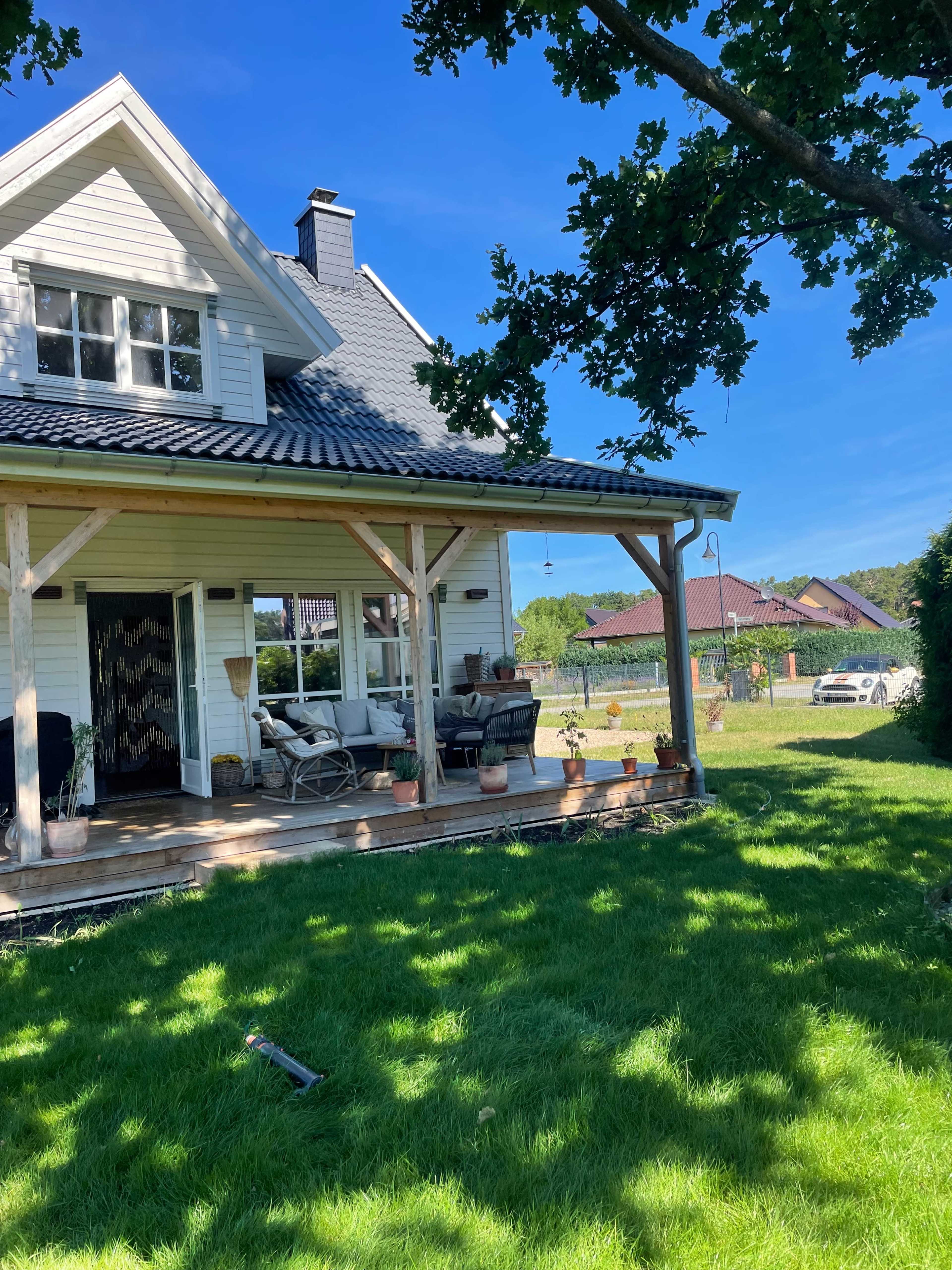 A white house with a porch is surrounded by green grass and trees under a clear blue sky.