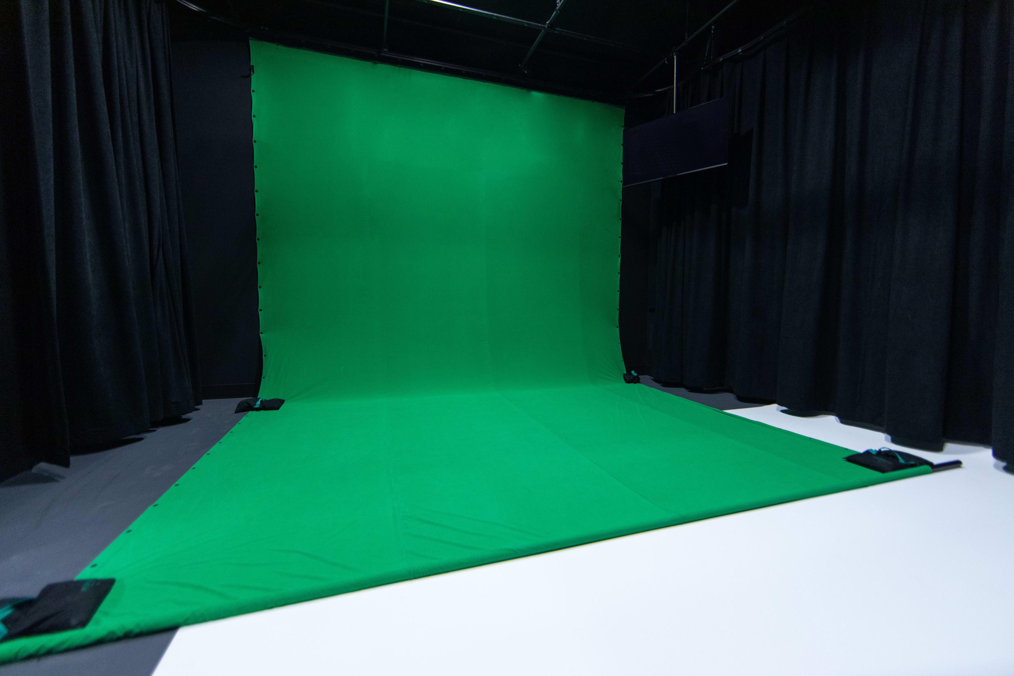 A green screen setup in a studio, surrounded by black curtains and a white flooring section.