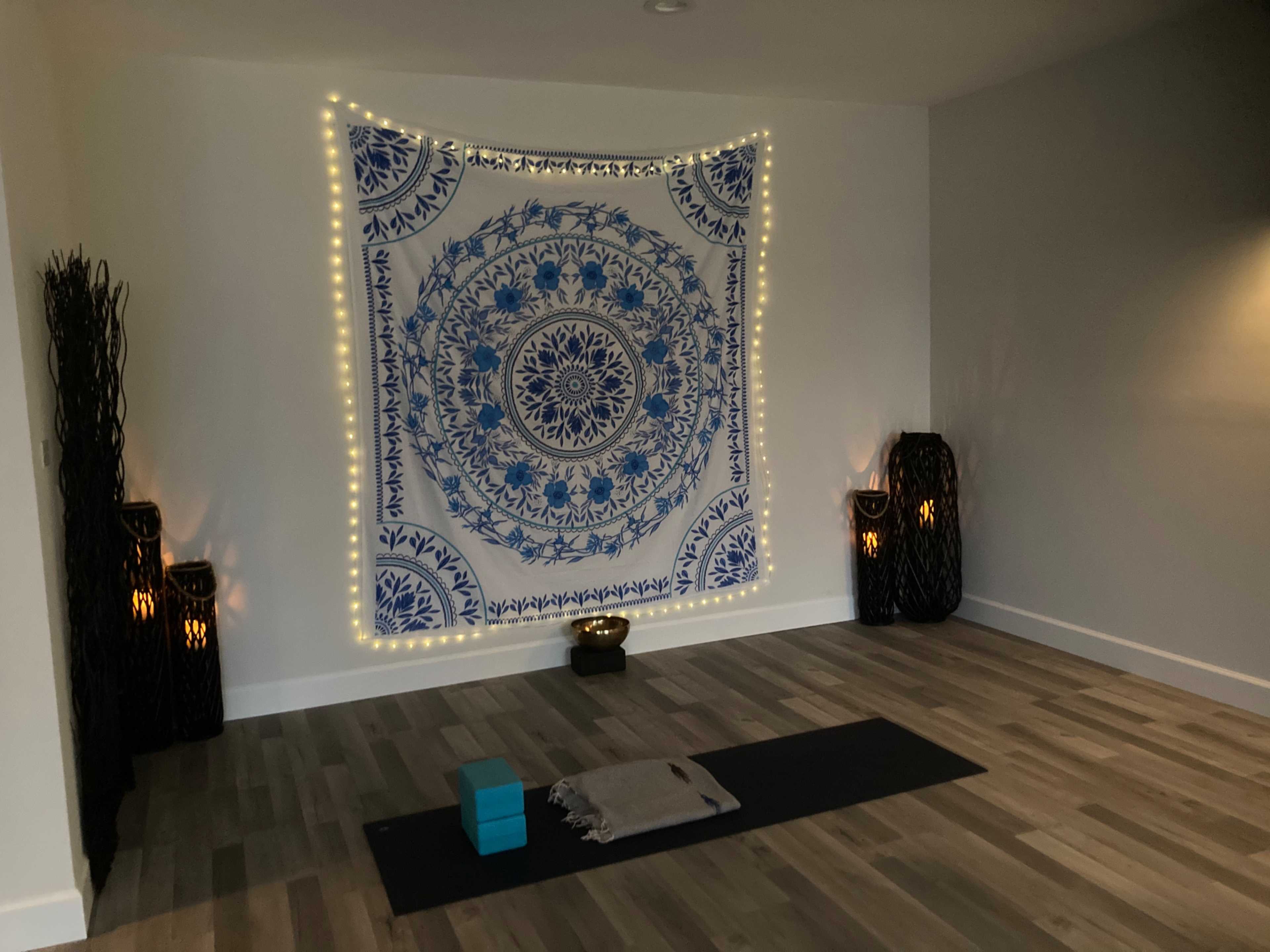 A serene yoga studio features a large blue tapestry with lights, flanked by decorative pillars and a yoga mat centered on the floor.