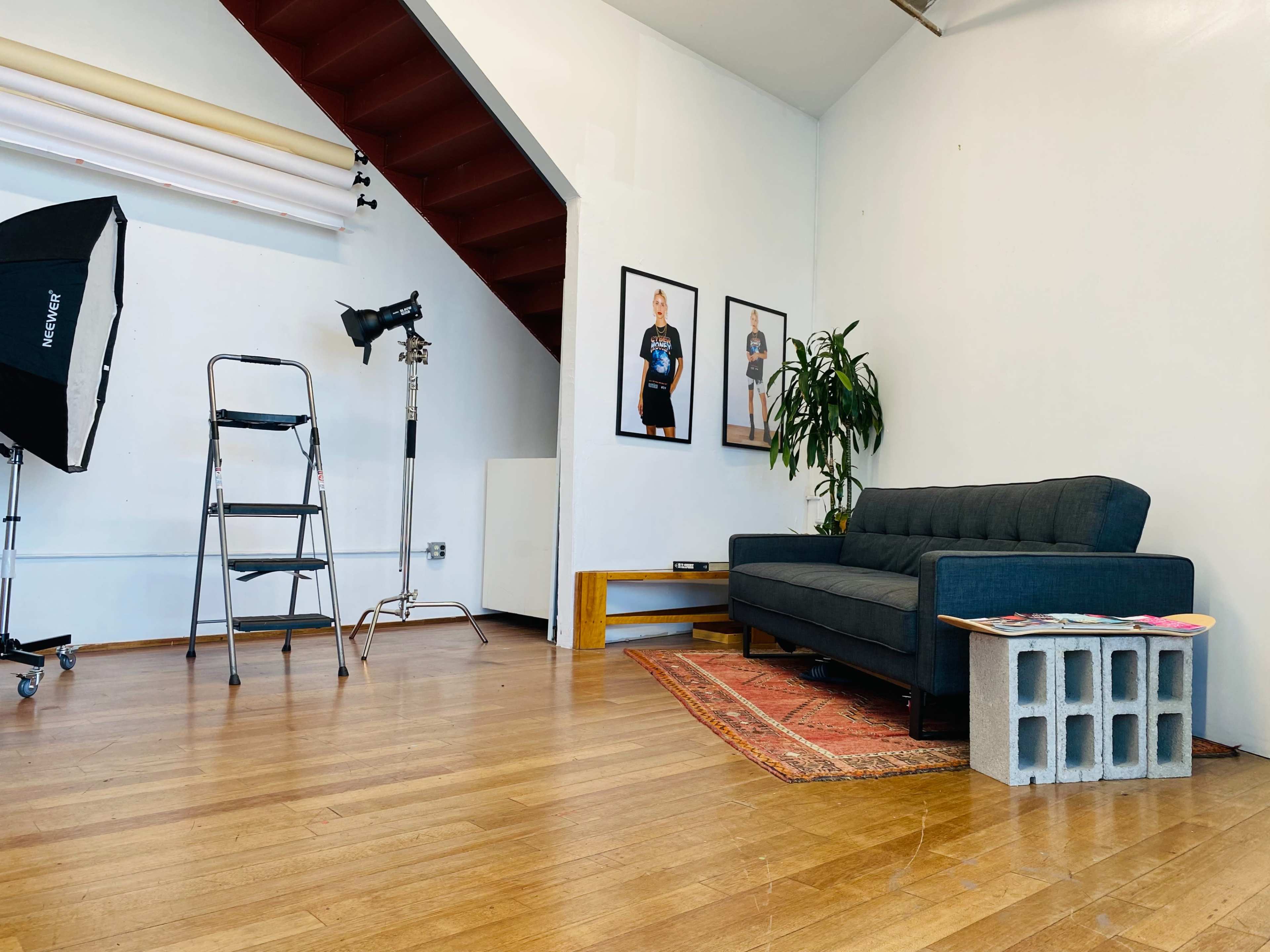 A studio interior featuring a dark couch, a stairwell, a potted plant, and a photography backdrop setup with lighting equipment.