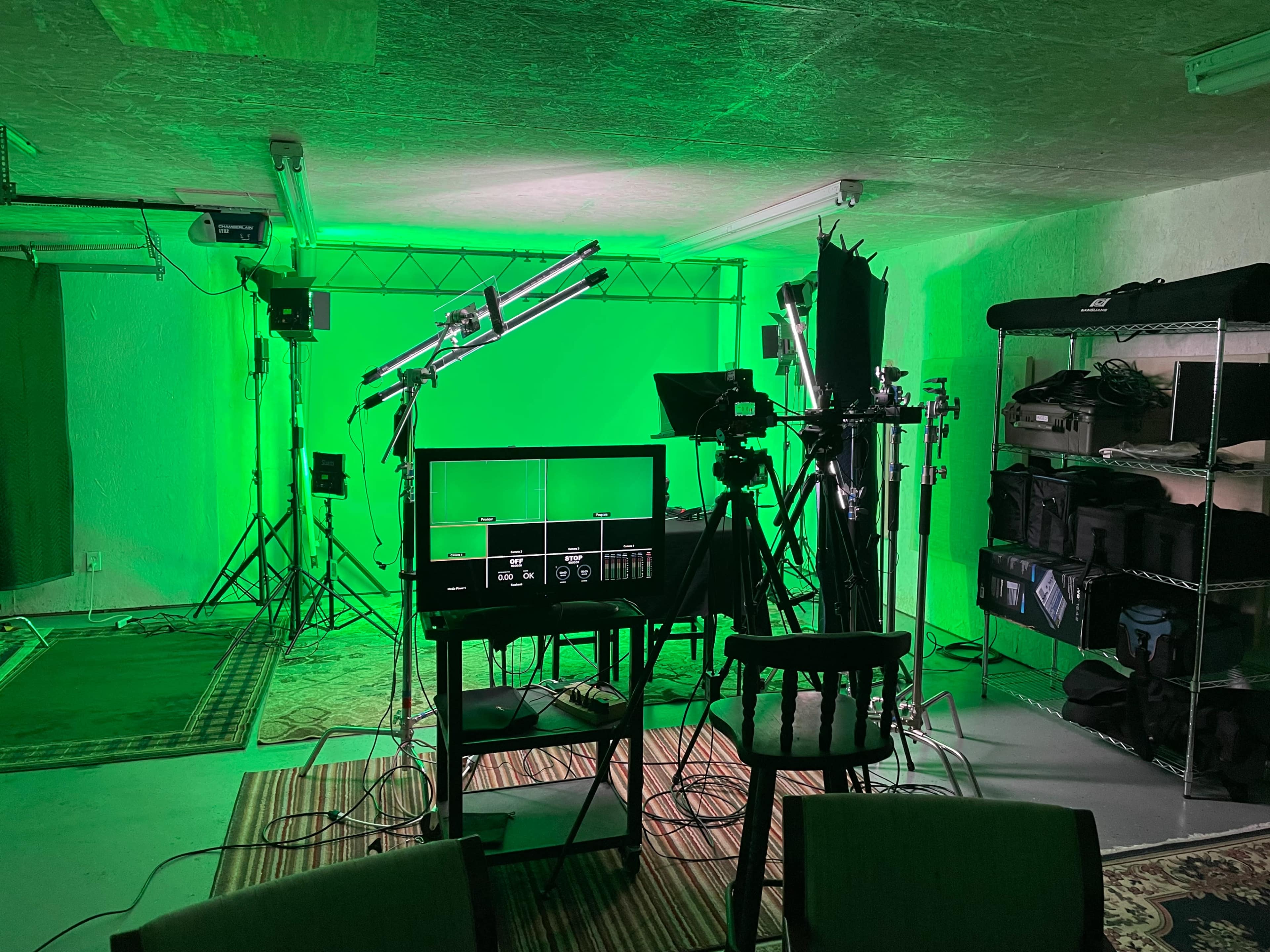 A green-lit studio setup with camera equipment, lighting rigs, and various props arranged in a spacious room.